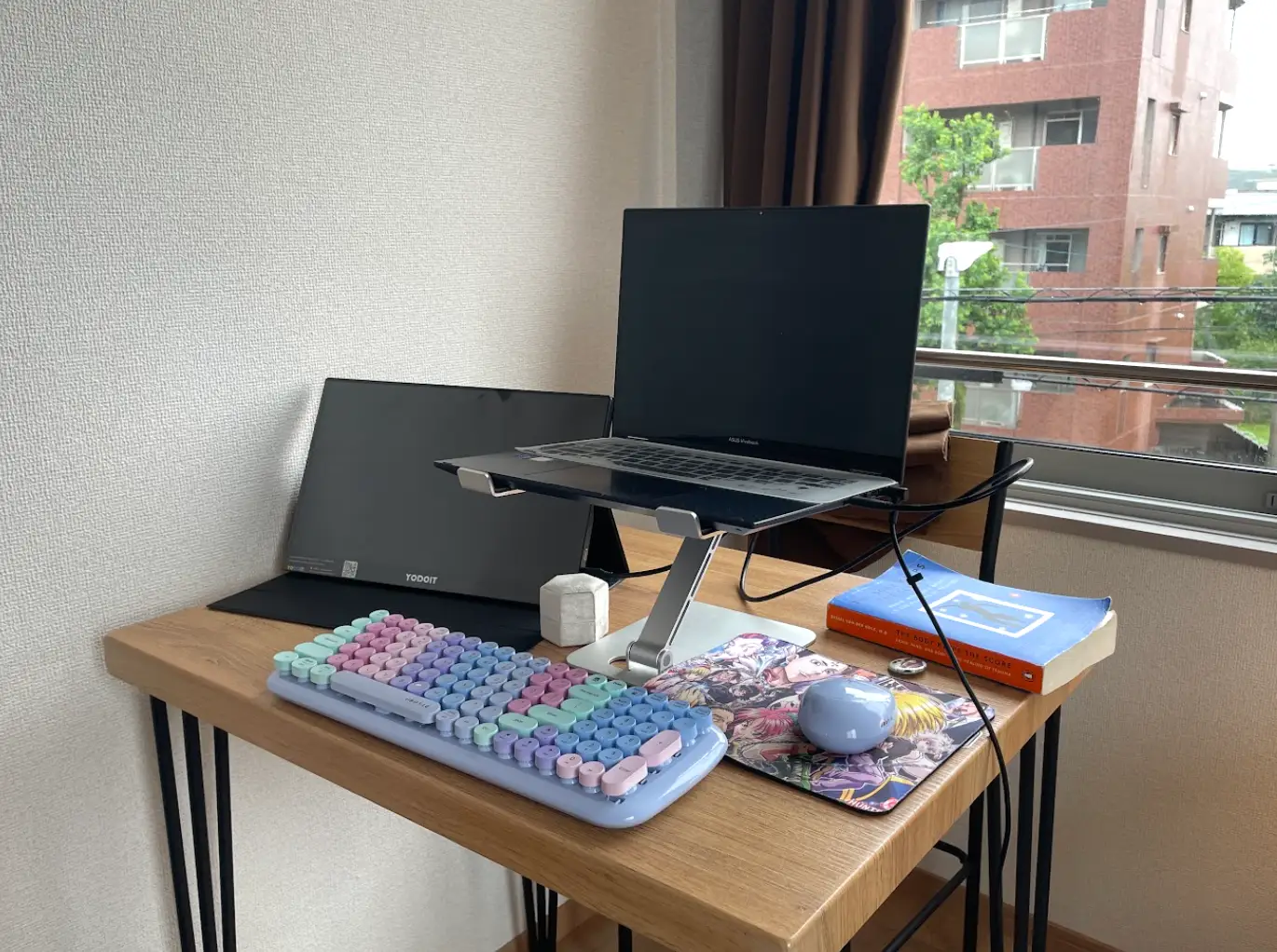 The writer's desk setup, with a laptop, keyboard, portable monitor, mouse, and paperback book.