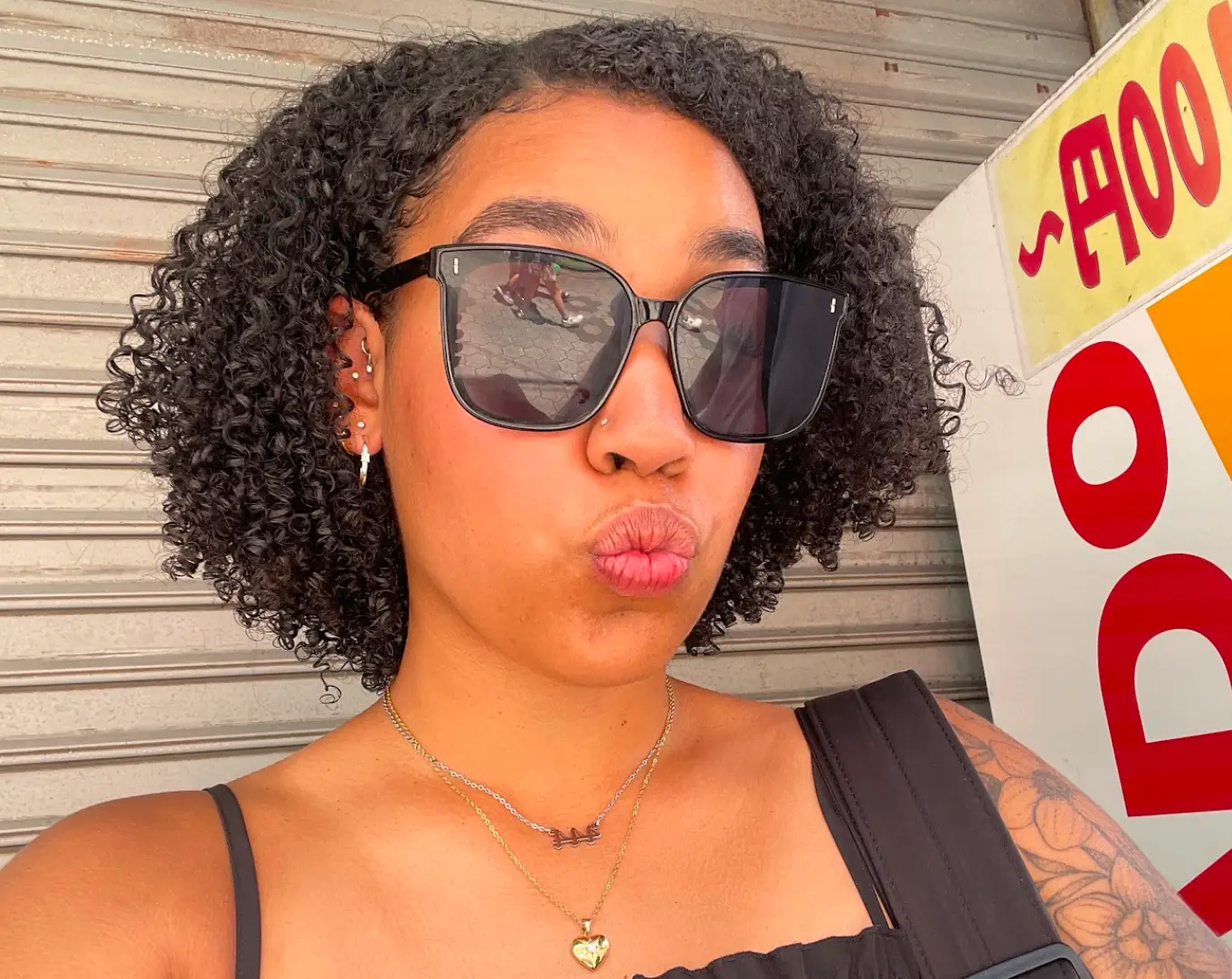 The writer posing for a selfie, wearing black sunglasses and showcasing curly hair.