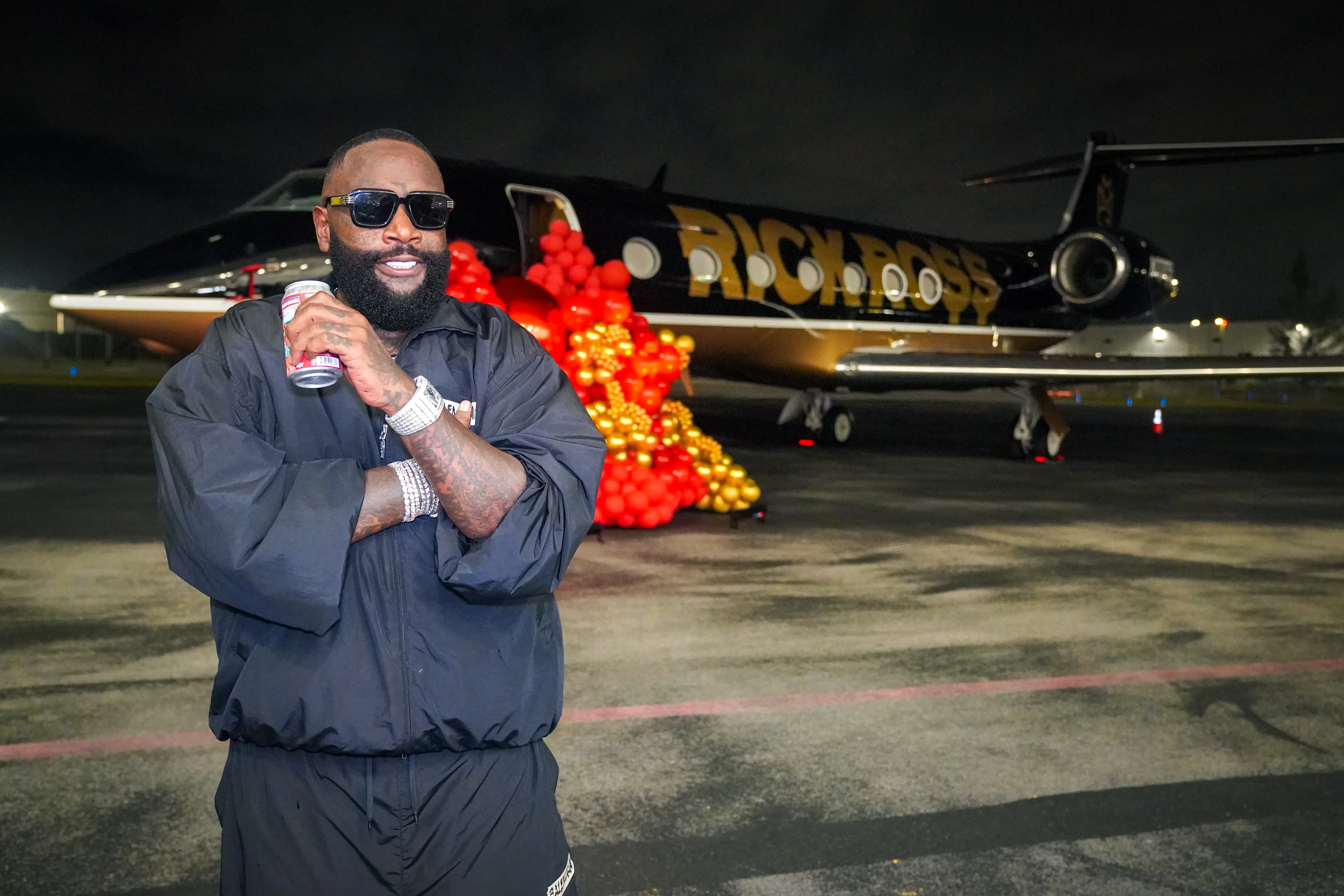 Rapper Rick Ross is standing outside his private jet.