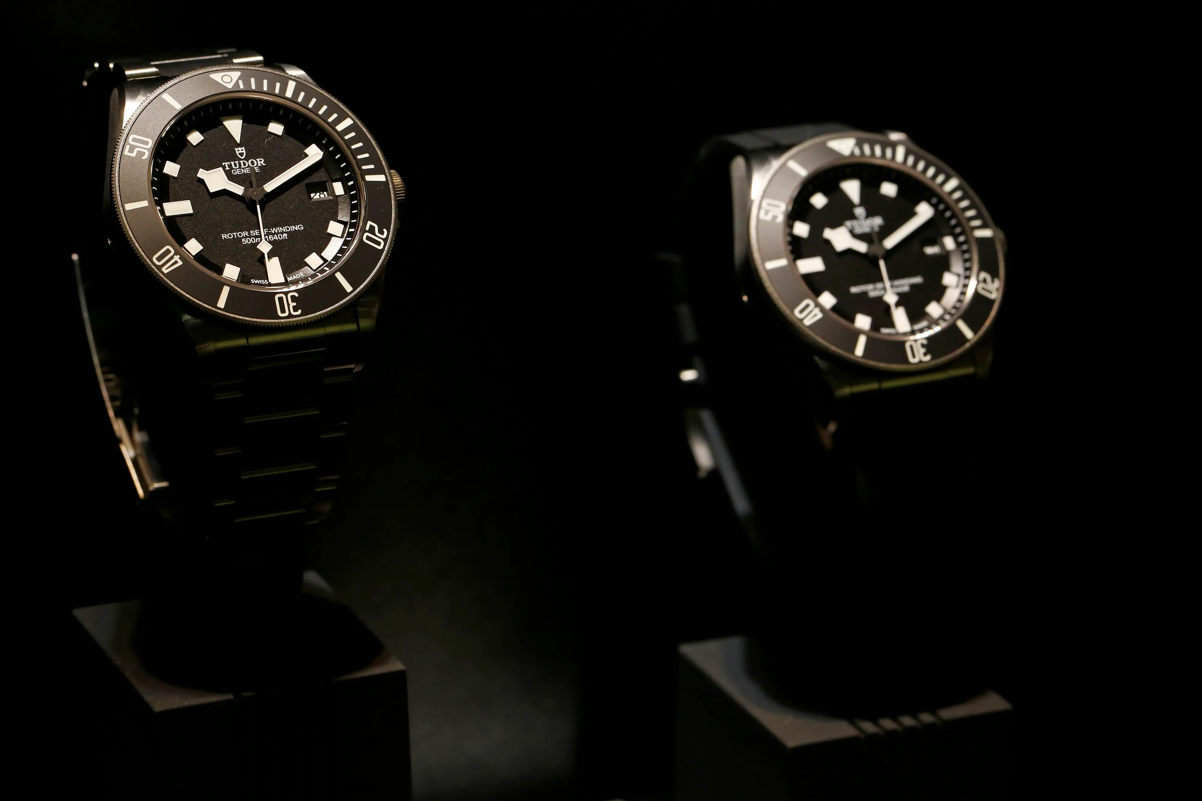 Two Tudor wristwatches are displayed on stands against a dark showroom background.