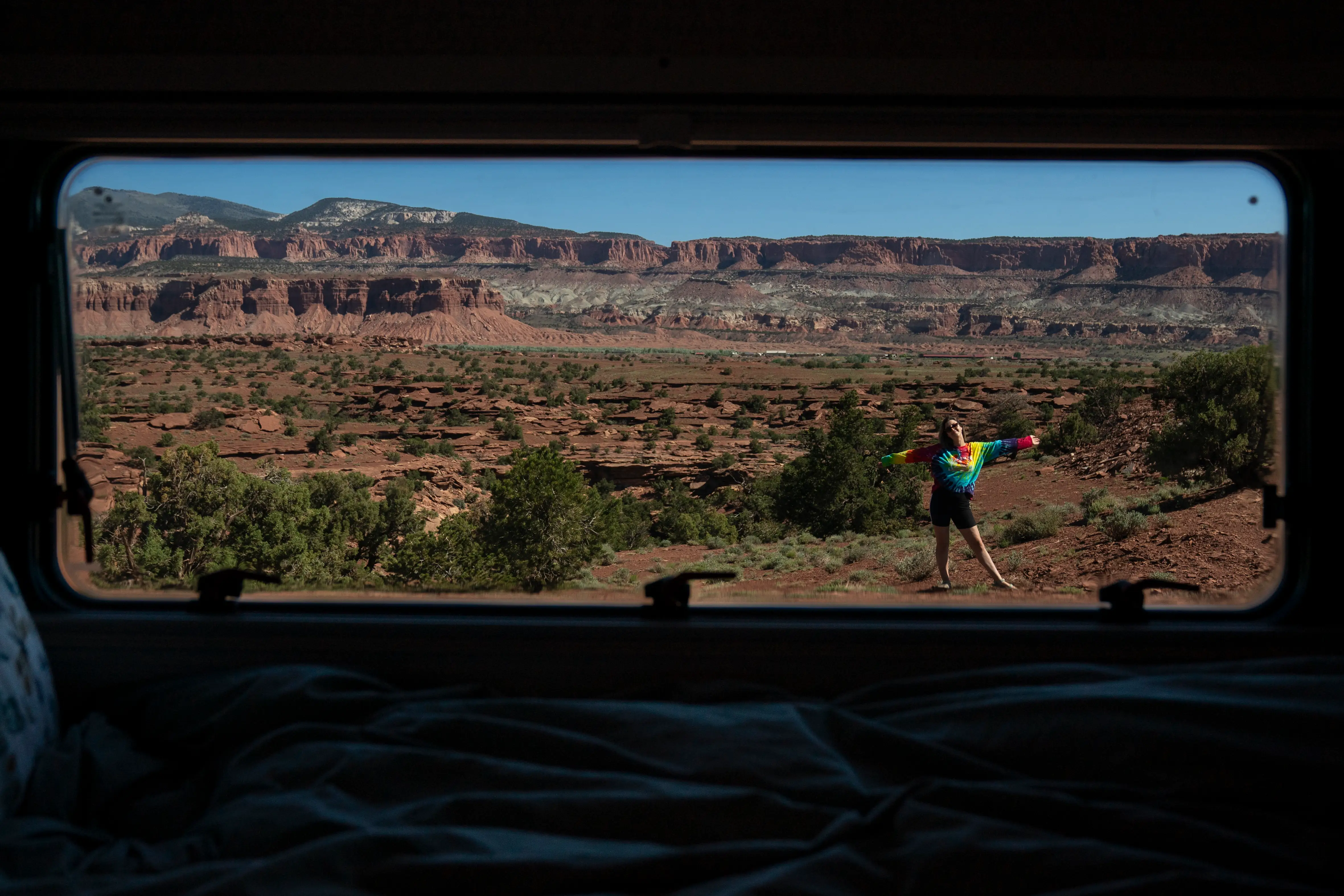 Sarah Silbiger in a colorful shirt stands outside a vehicle window overlooking a red rock desert canyon.