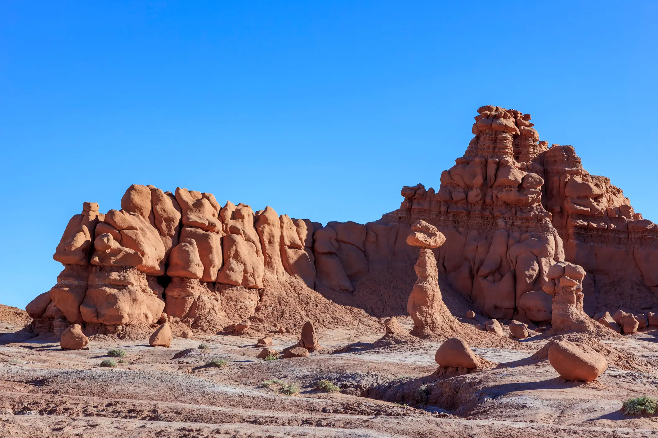 Red sandstone hoodoos and eroded rock formations rise from a desert landscape at Goblin Valley State Park under a clear blue sky.