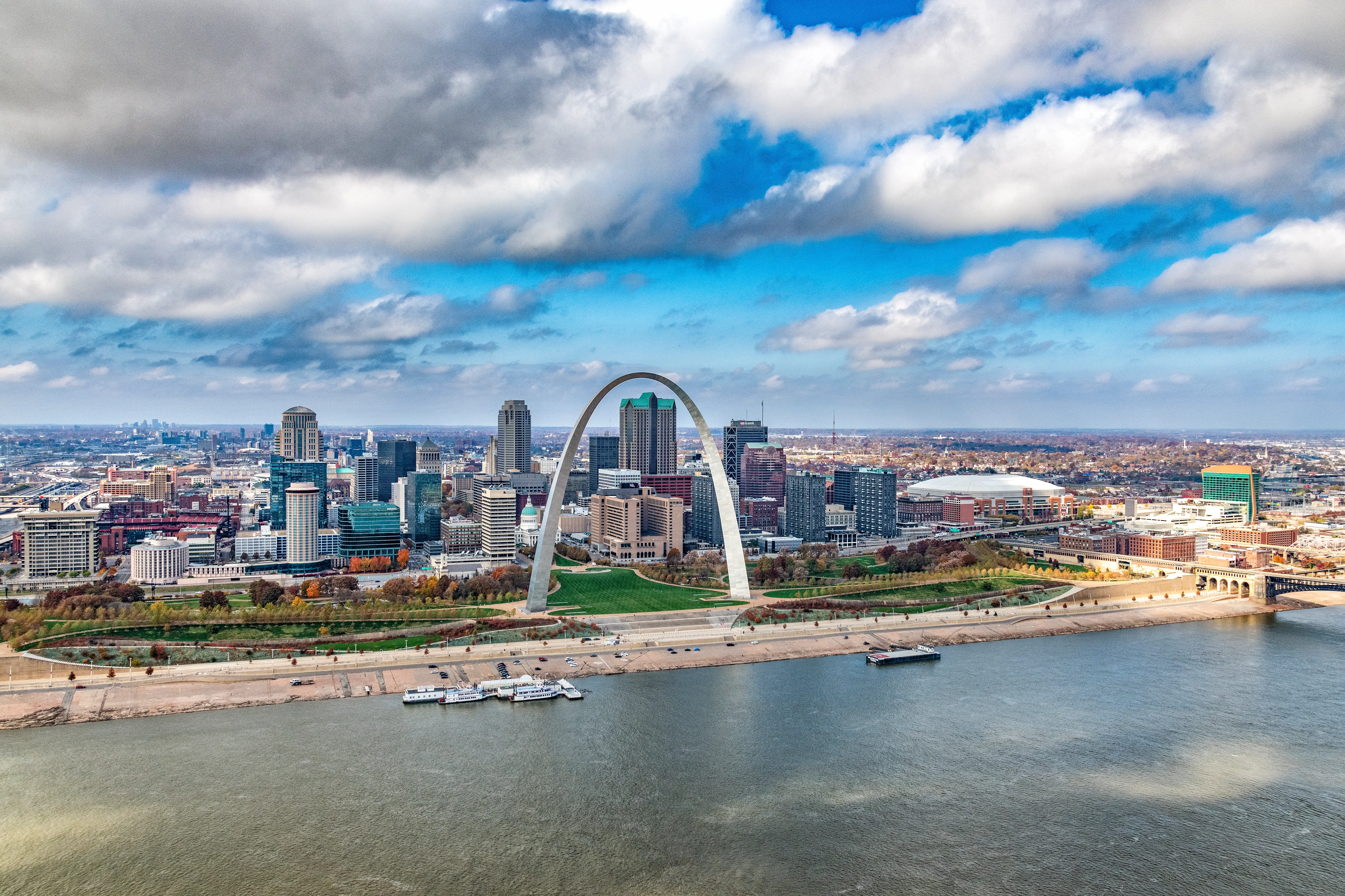 St. Louis skyline with the Gateway Arch beside the Mississippi River under a partly cloudy sky.