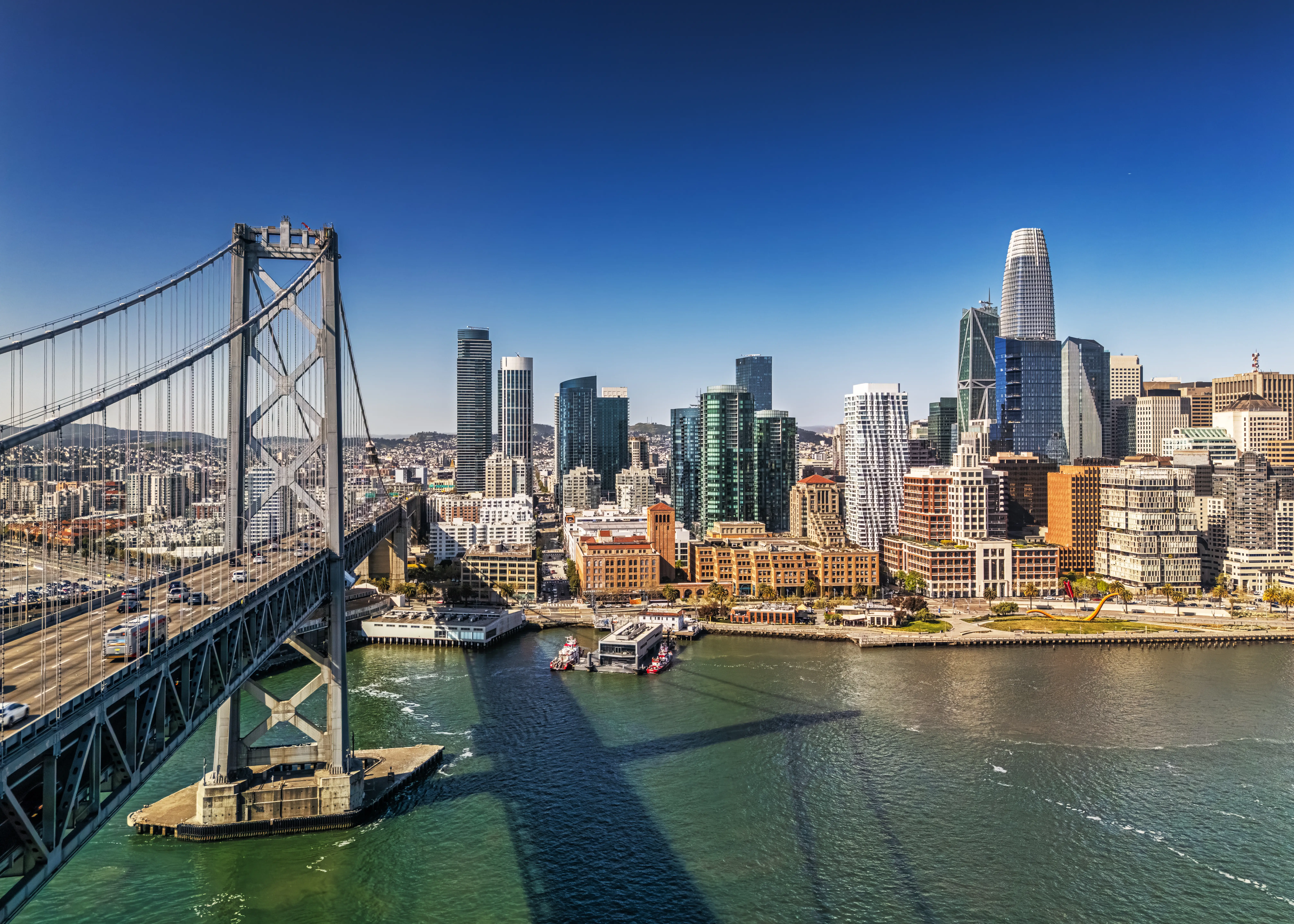 San Francisco skyline and waterfront seen beside the Bay Bridge under a clear blue sky.