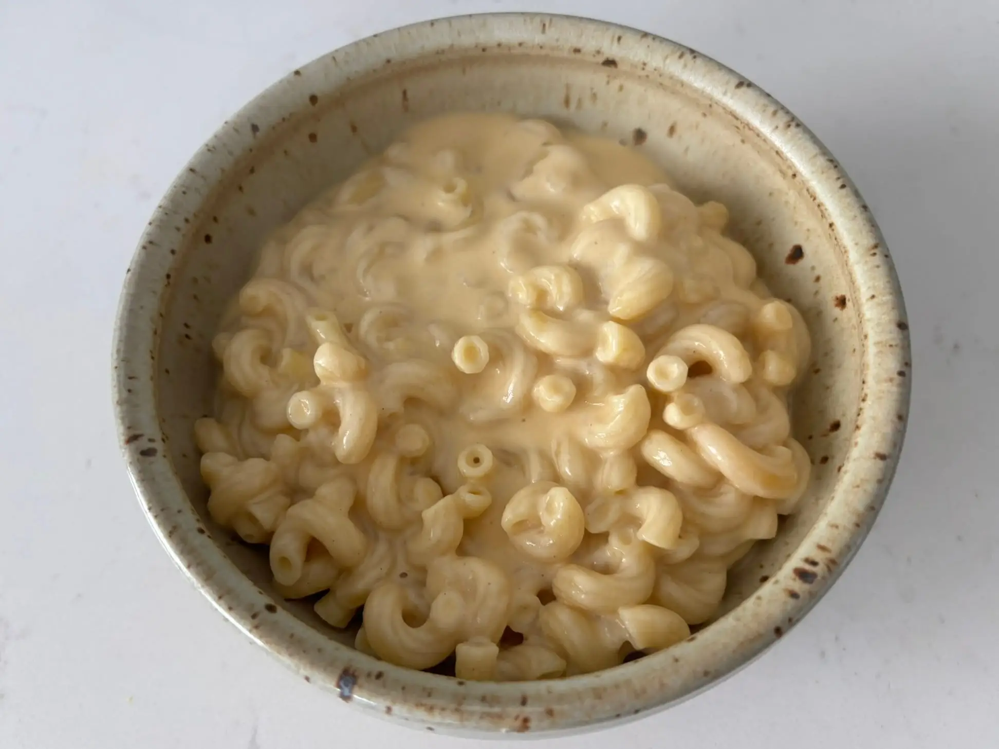 Creamy elbow macaroni sits in a speckled ceramic bowl on a light countertop.