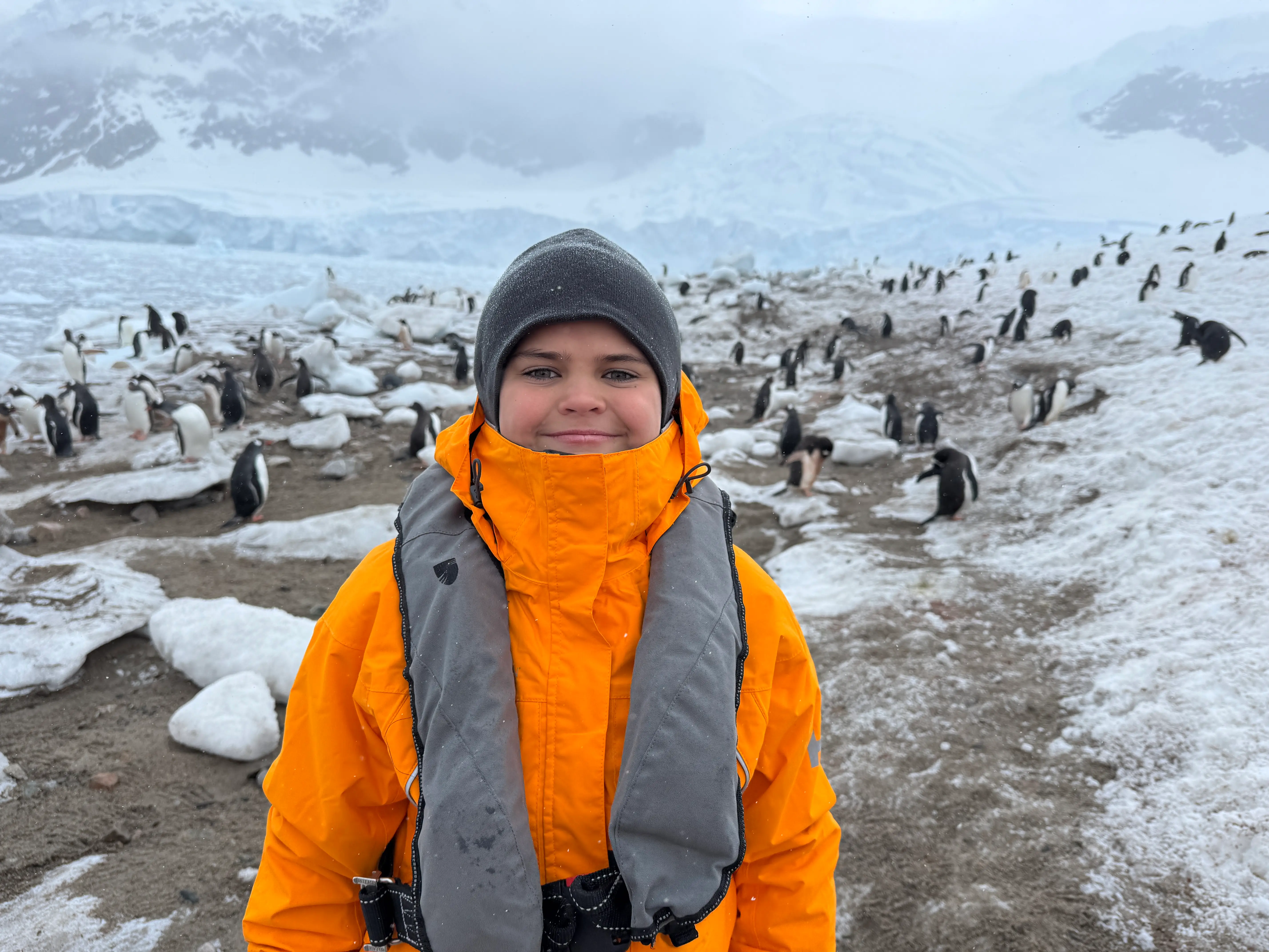 Kid in winter coat smiling near penguins in Antarctica