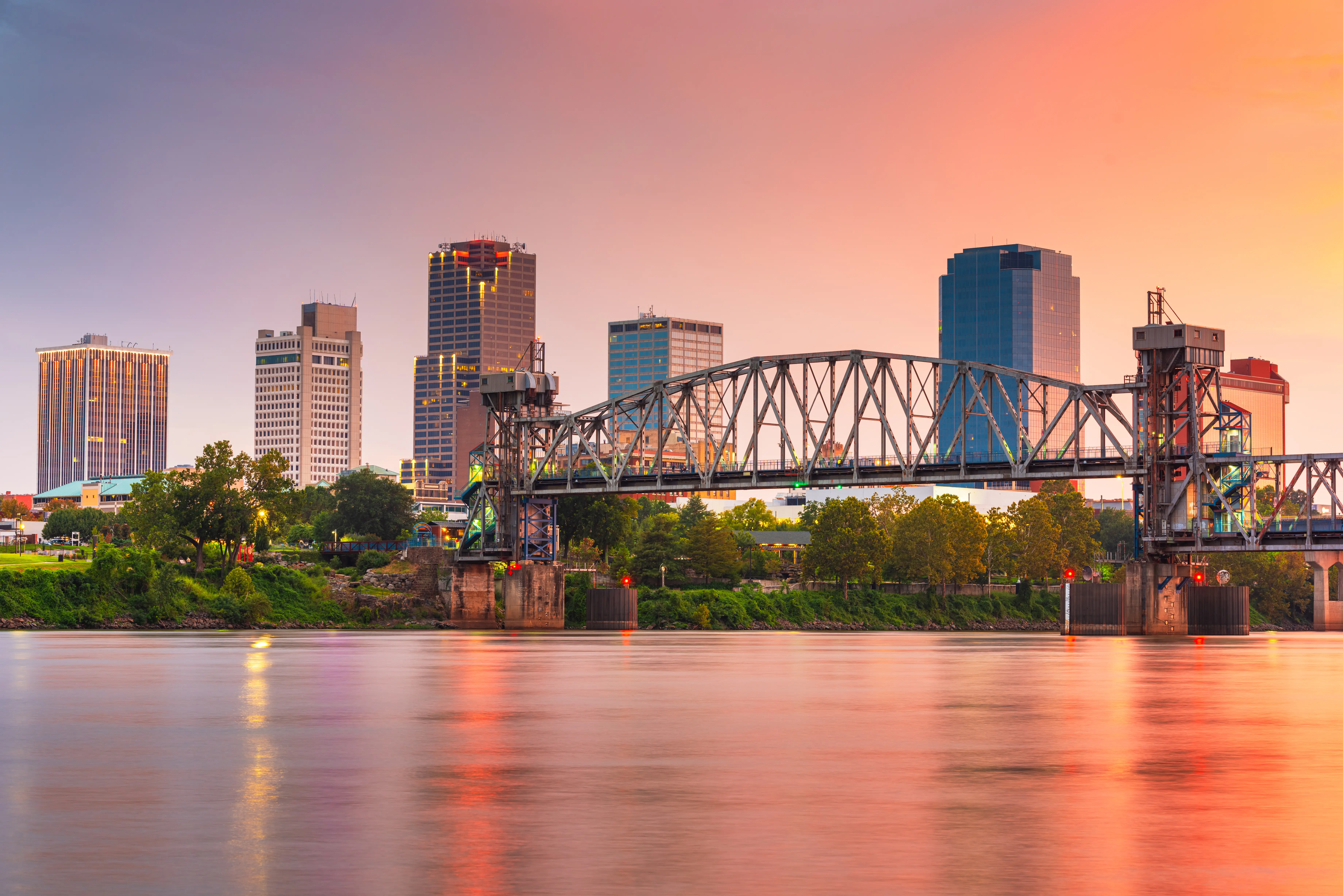 Downtown Little Rock skyline and truss bridge reflected in the Arkansas River at sunset.