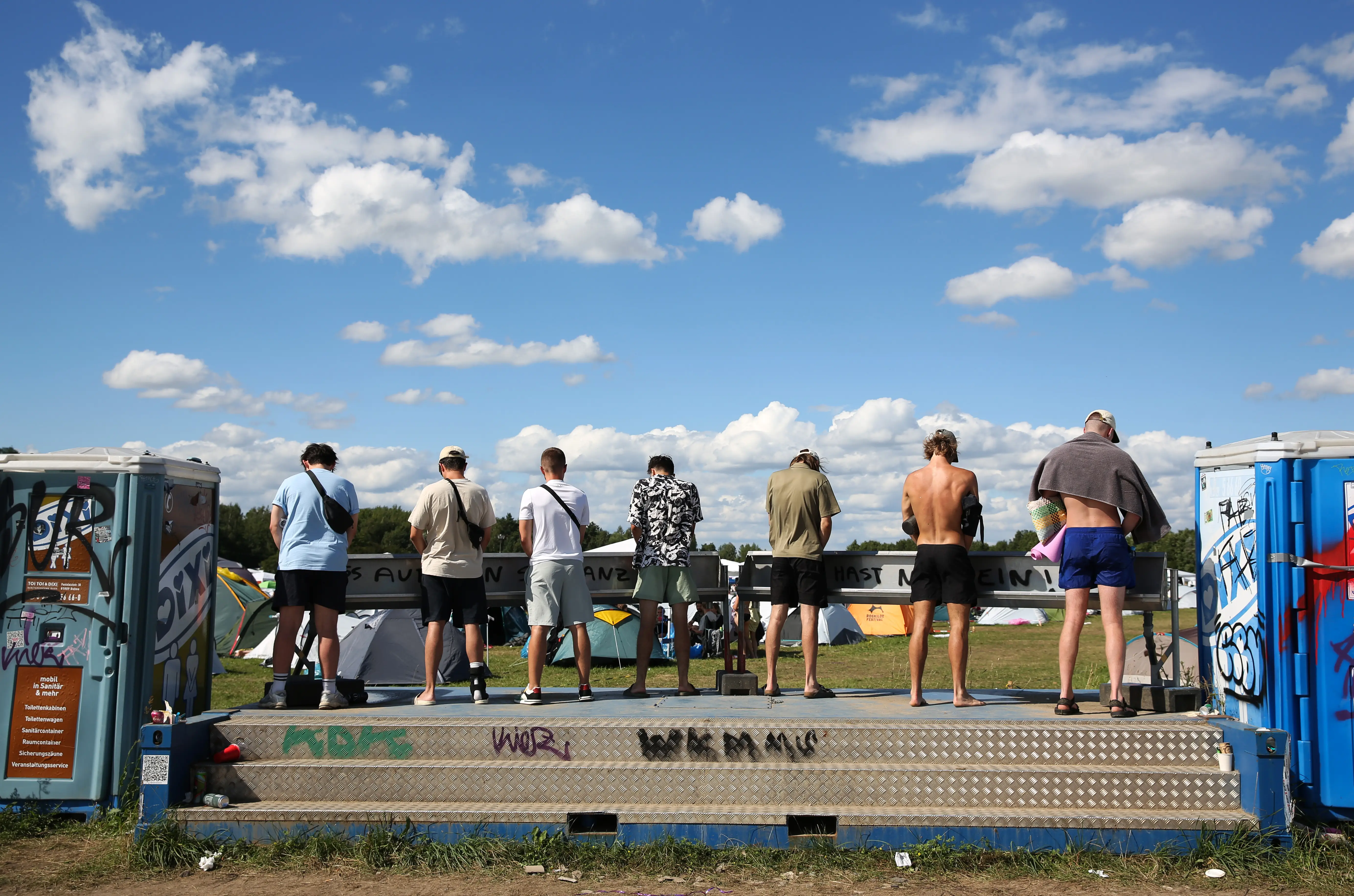 Men stand at an outdoor urinal.