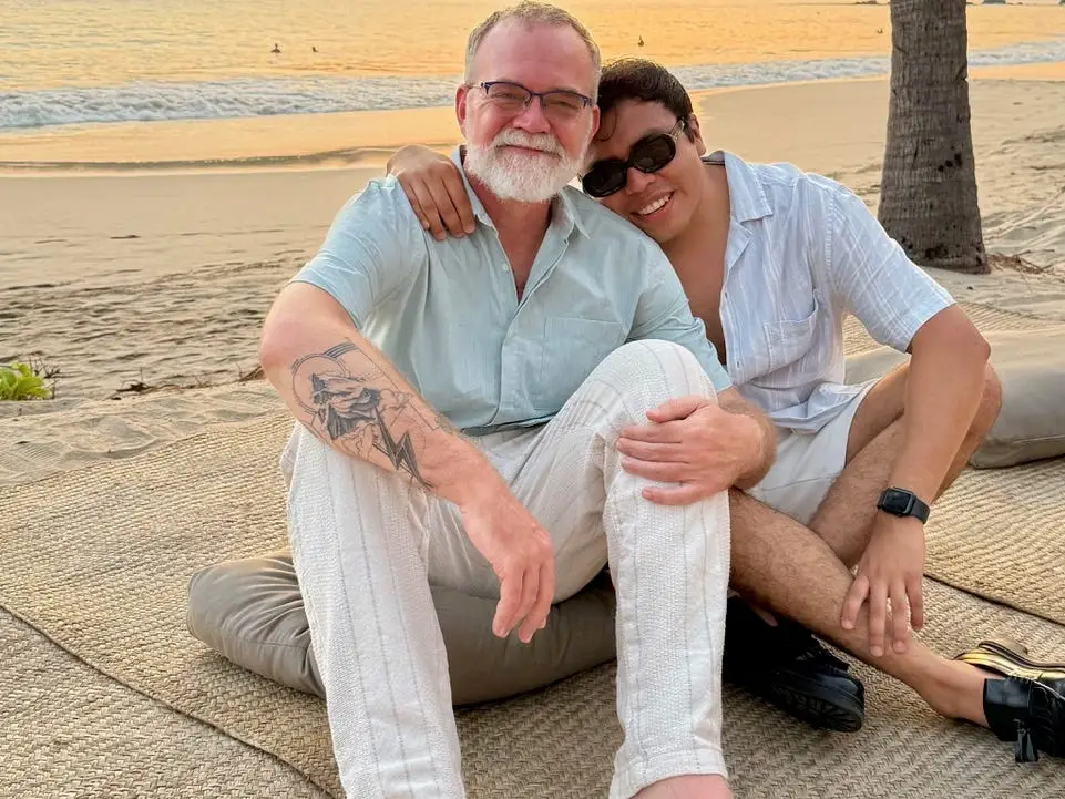 Bil Browning and his partner sitting near a beach embracing