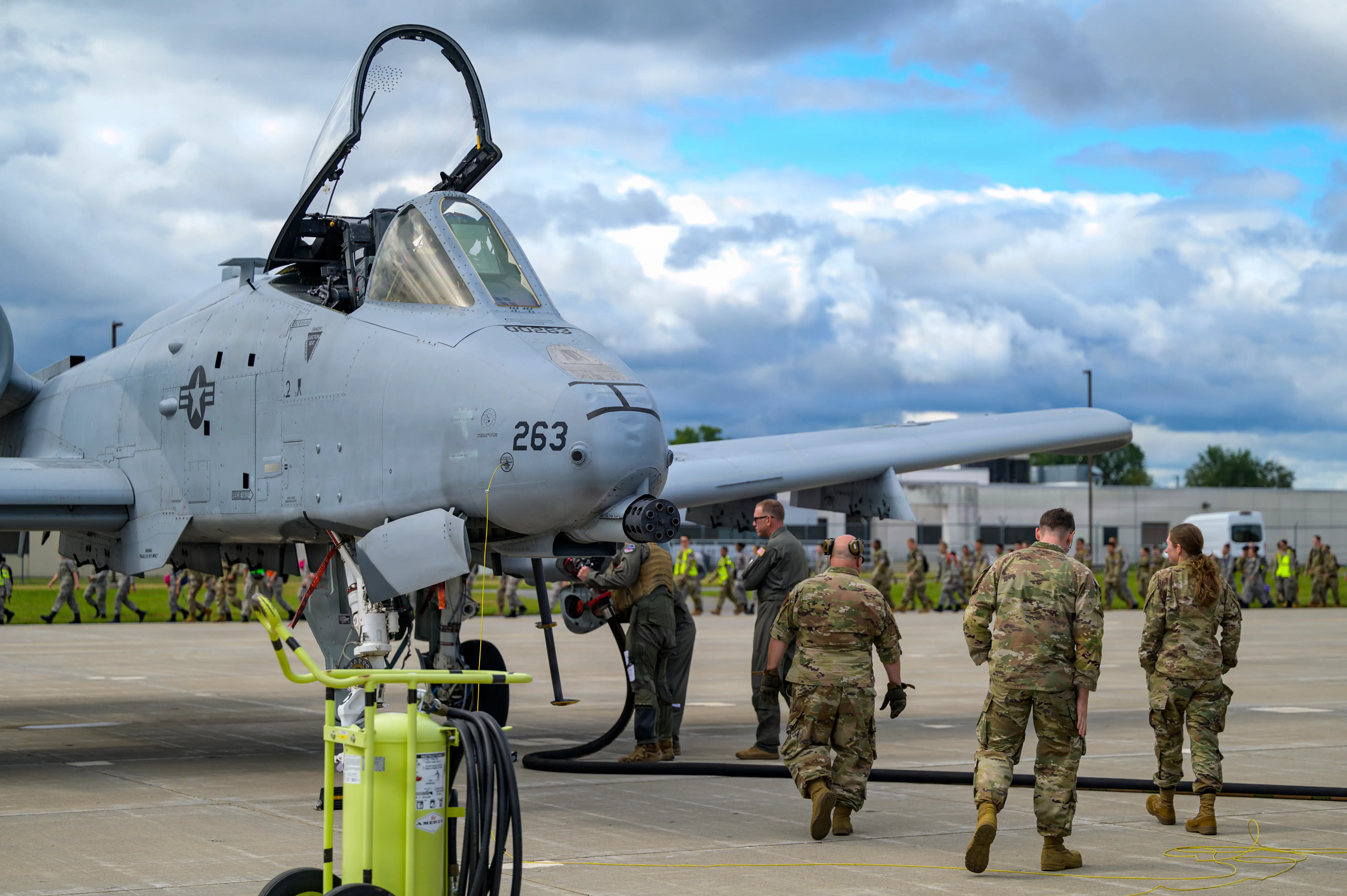 A U.S. Air Force A-10 aircraft sits on a tarmac with its cockpit open as uniformed personnel walk nearby.