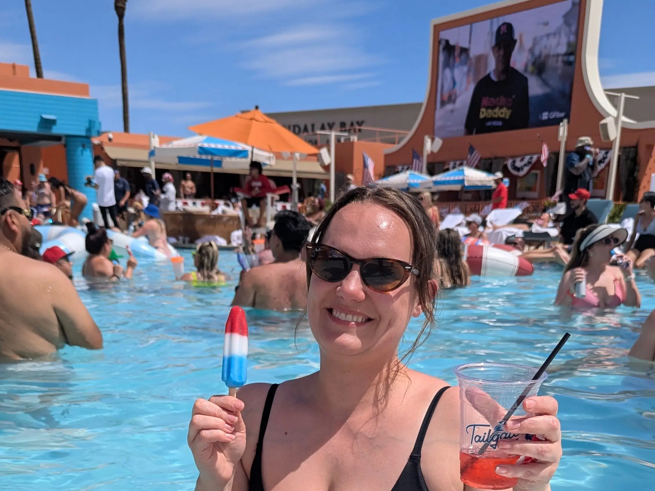 Emy holds an ice pop in one hand and a drink in the other while enjoying the pool.