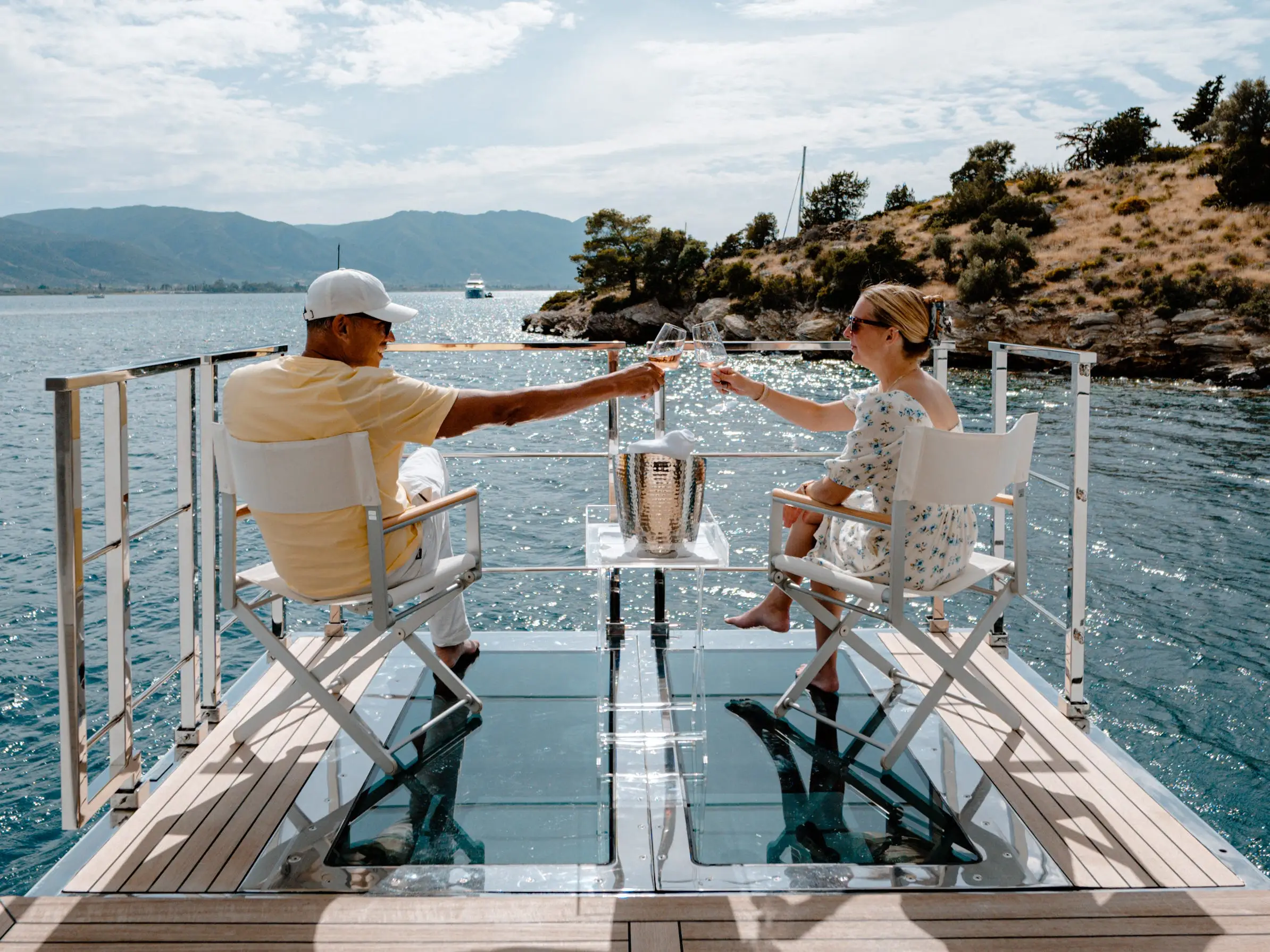 Woman and man cheers-ing with glasses on of yacht in front of water