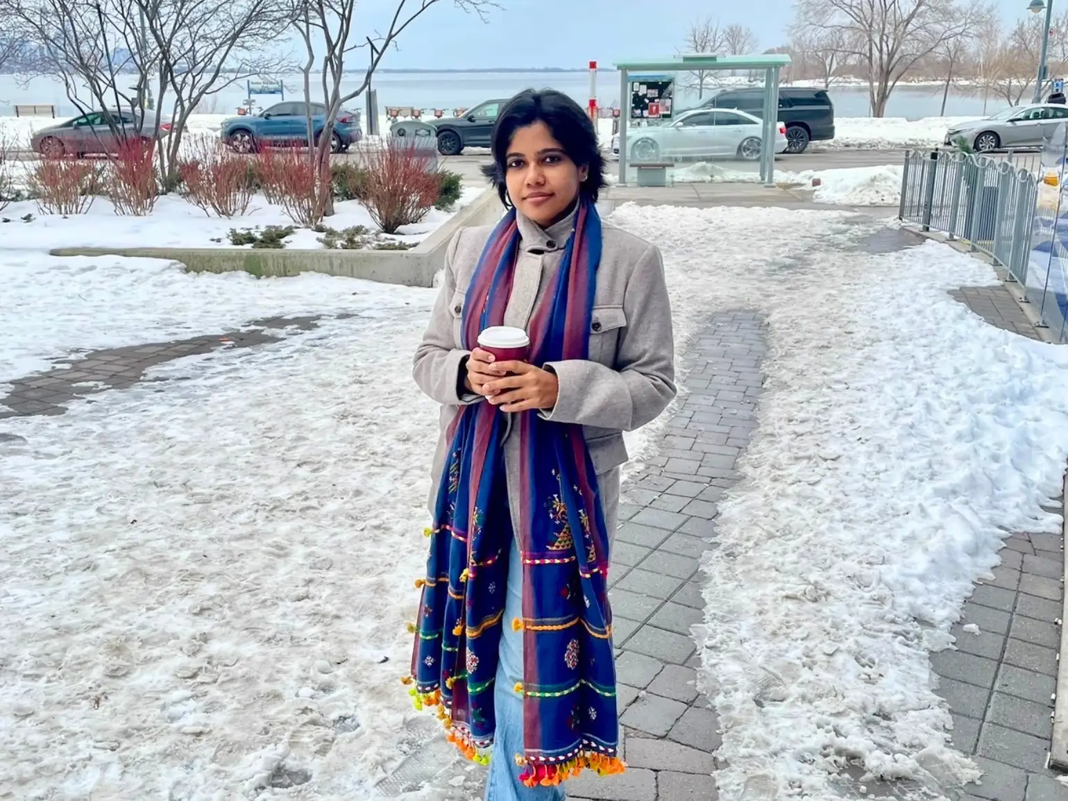 Shreya Mishra Reddy is standing on an icy road, holding a disposable coffee cup