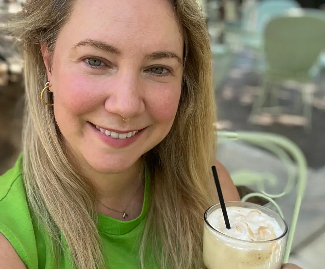 A close-up of the writer's face as she holds a coffee drink.