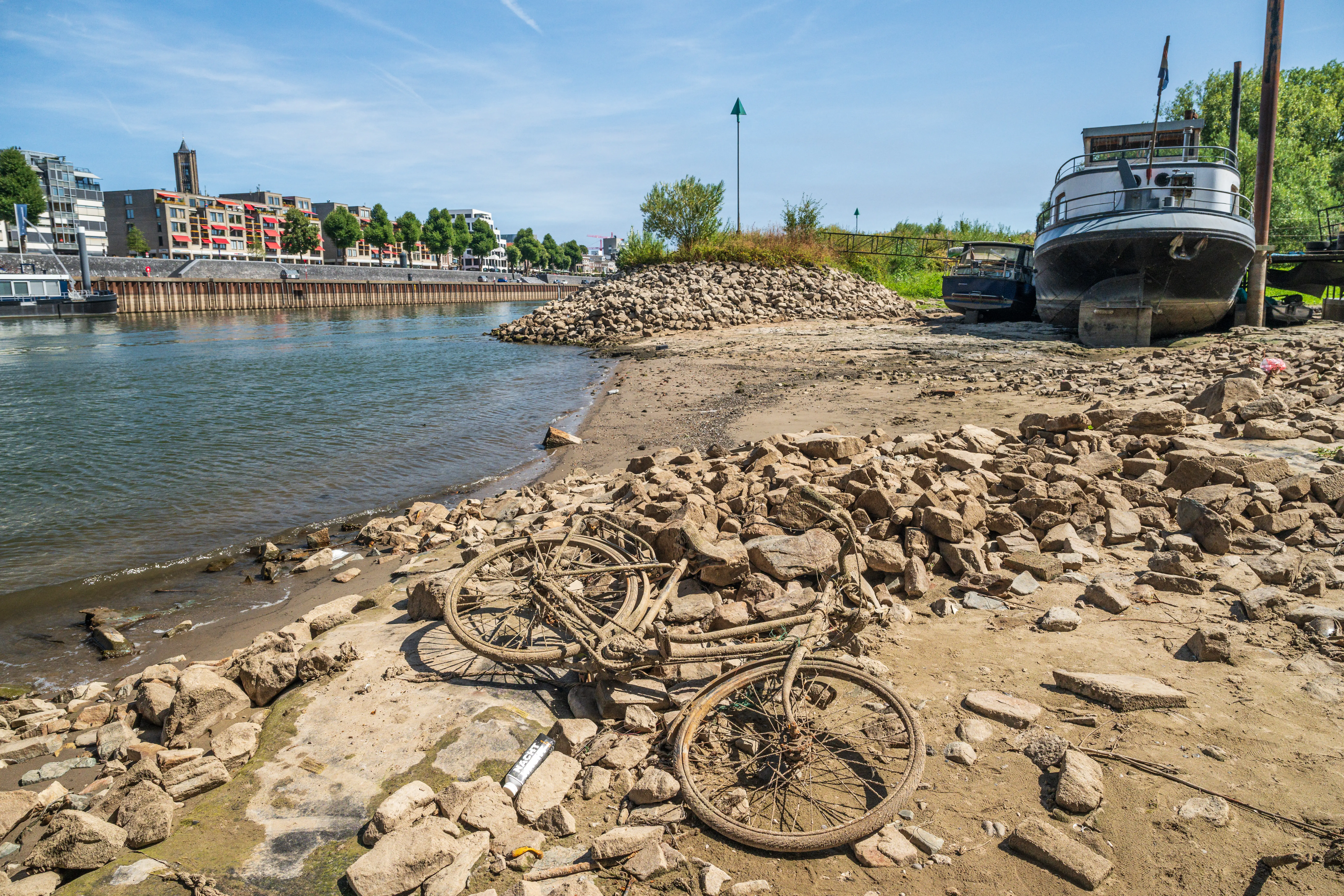 A mud-covered bike and stranded houseboat lay on a dried riverbed.