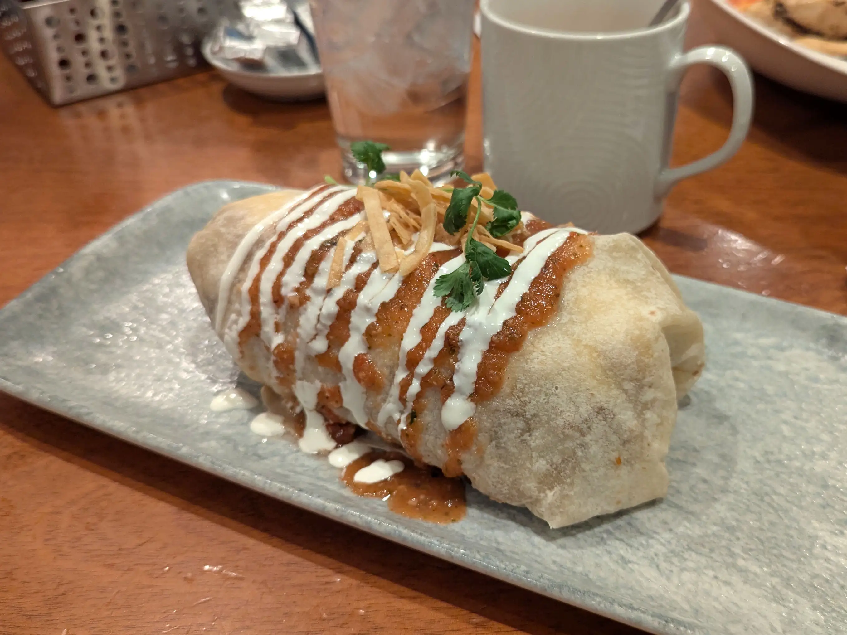 A burrito topped with sauce, crema, and tortilla strips.