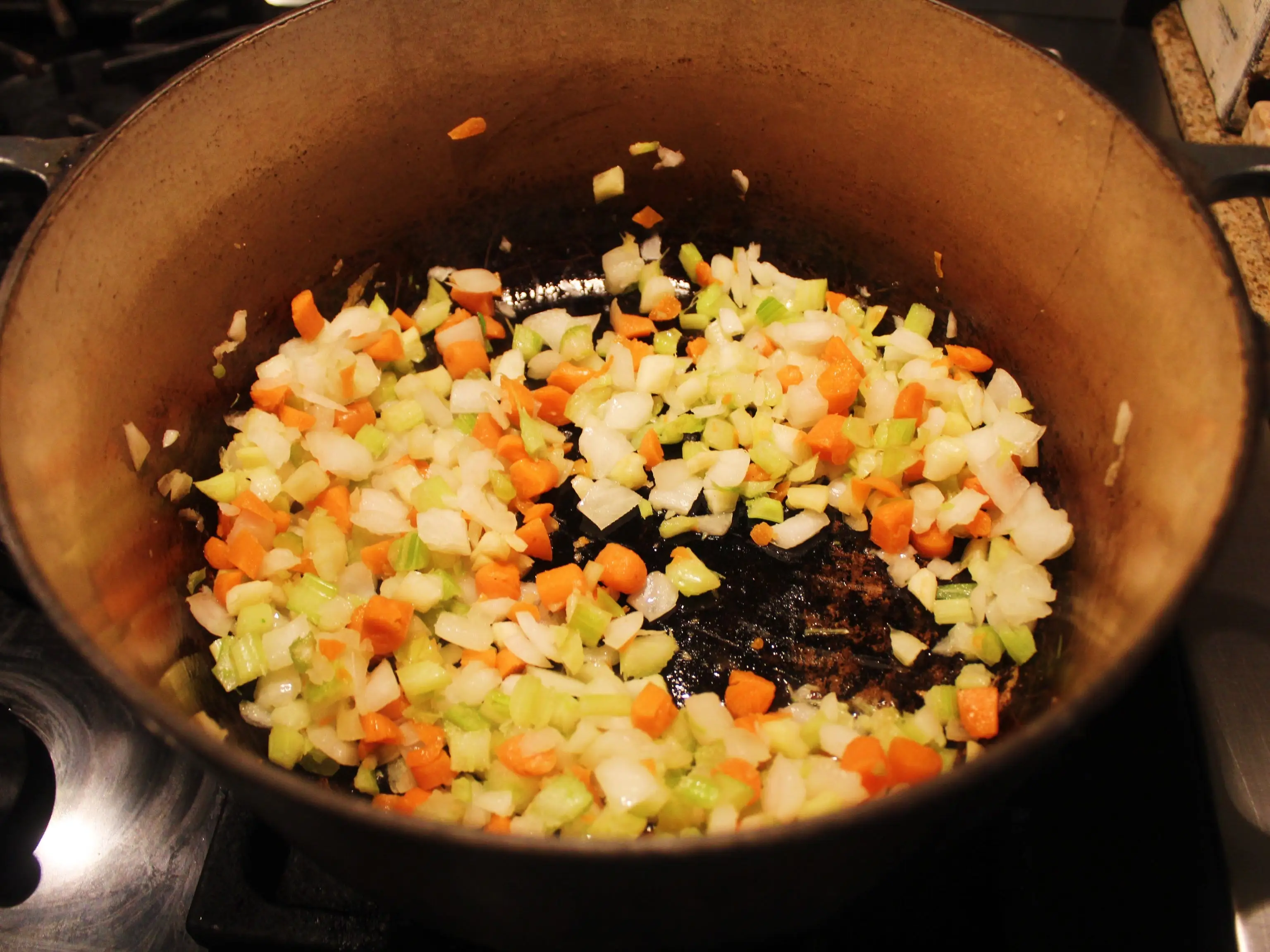 Chopped carrots, celery, and onions sauté in a large pot on a stovetop.