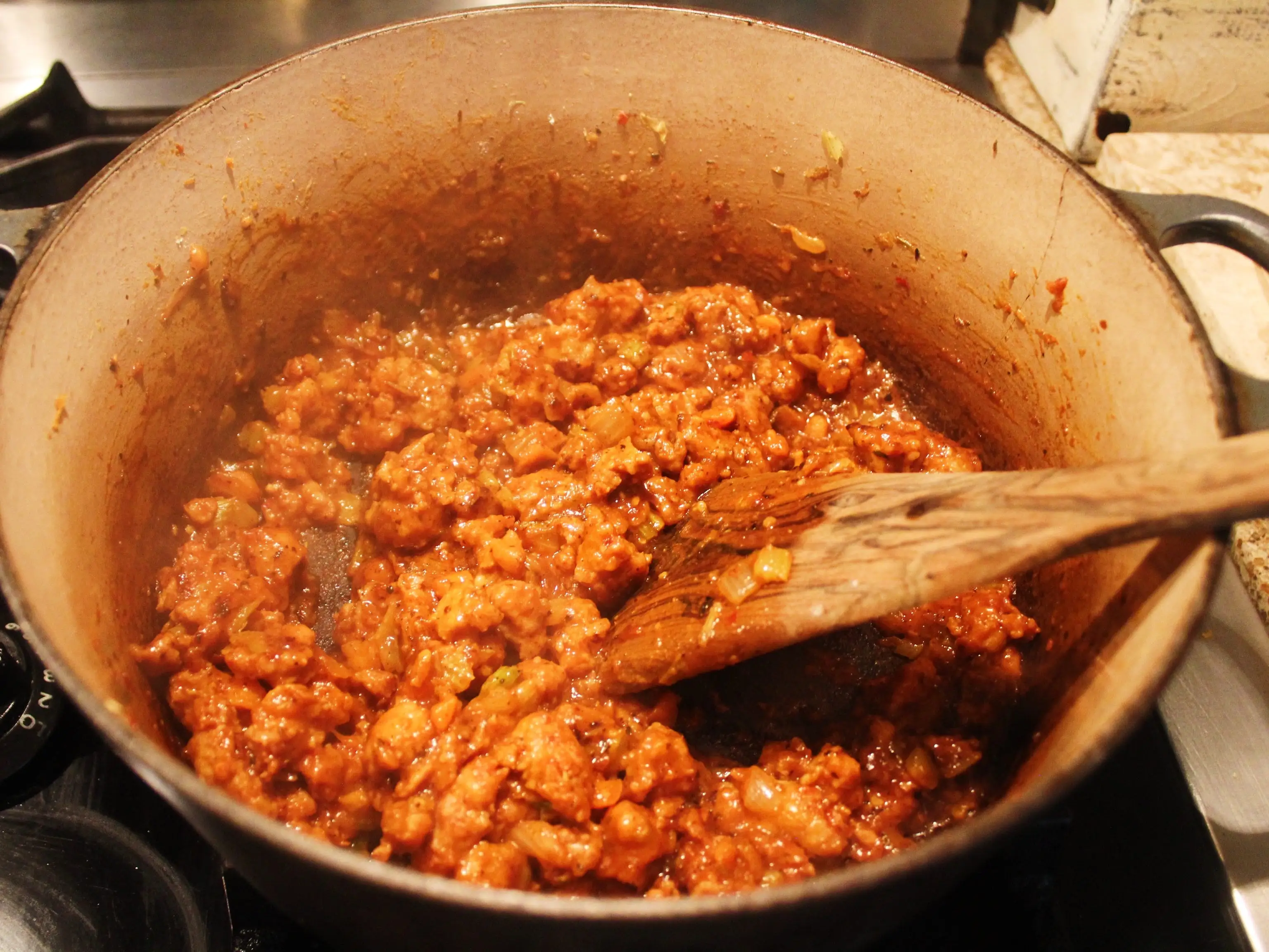 A wooden spoon rests in a large pot of simmering red sauce on a stovetop.