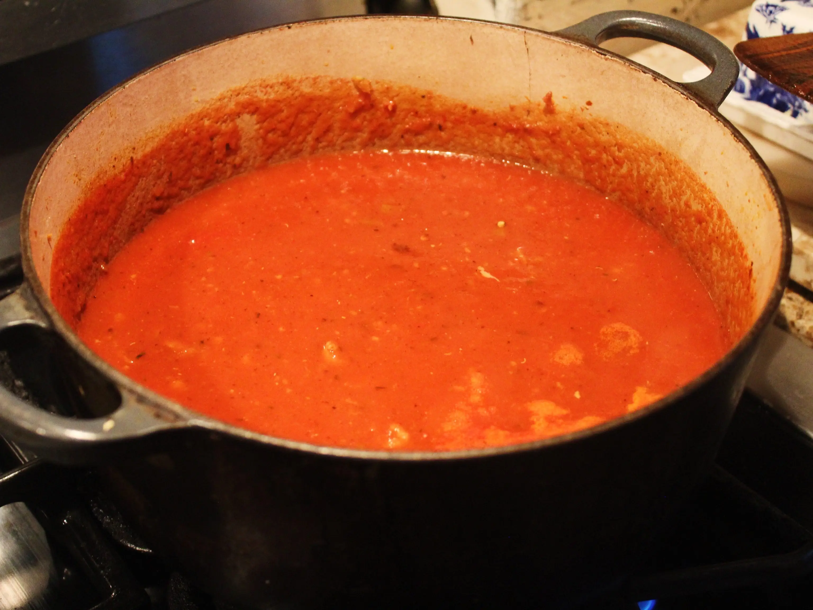 A large pot of red tomato sauce simmers on a stovetop burner in a kitchen.