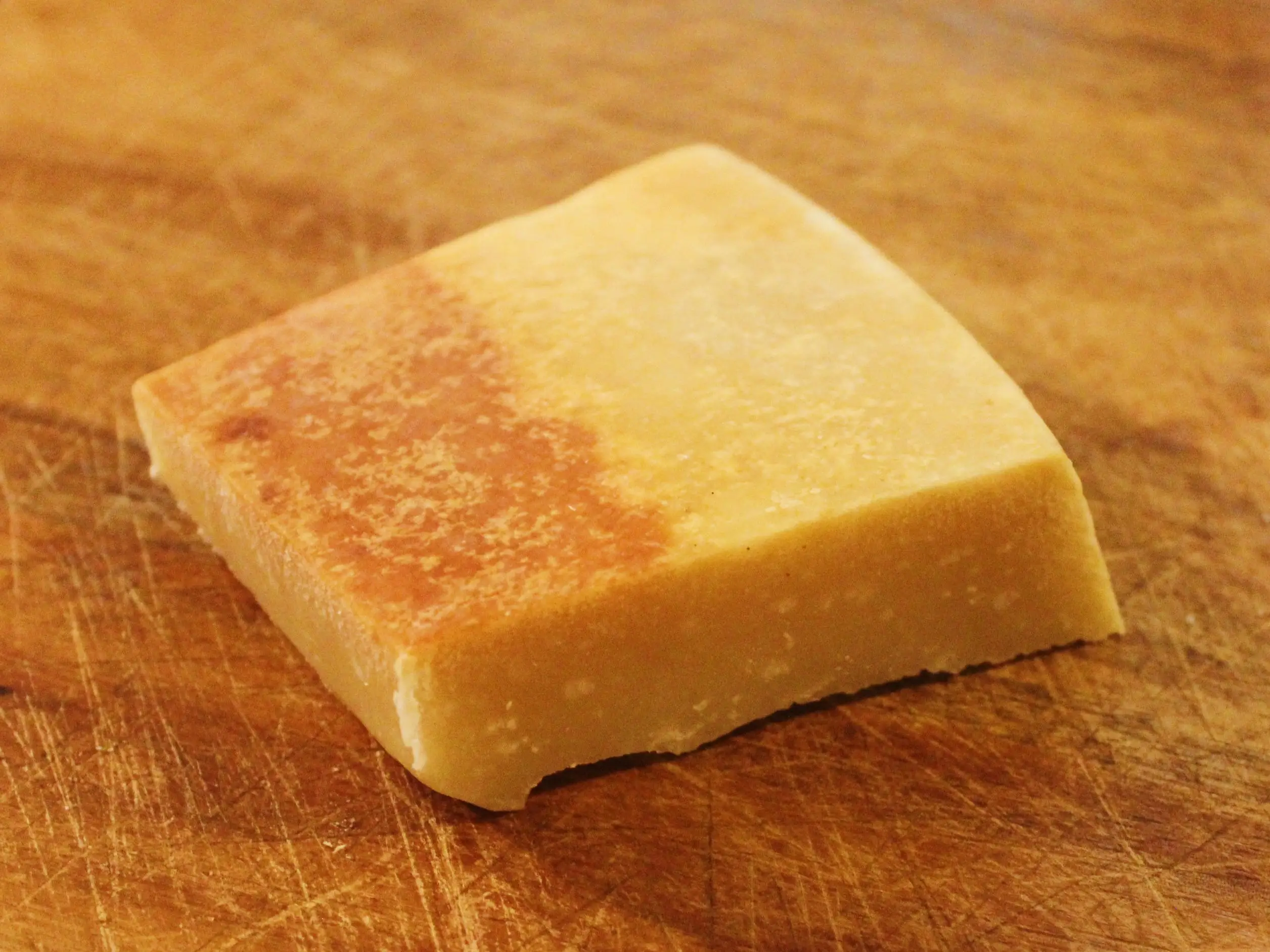 A rectangular block of yellow hard cheese rests on a scratched wooden cutting board.