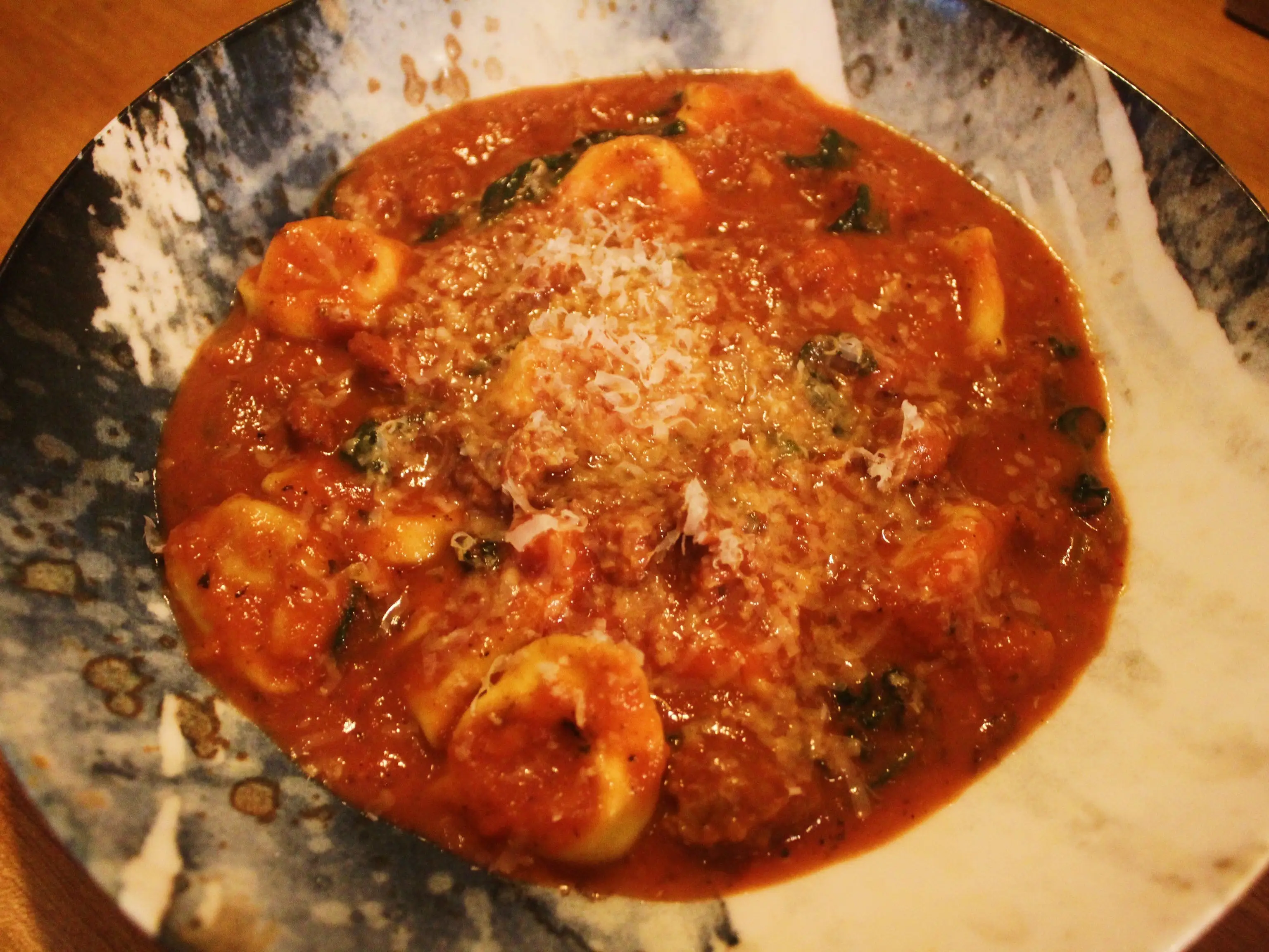 Tortellini in red tomato sauce with grated cheese served in a patterned bowl on a wooden table.