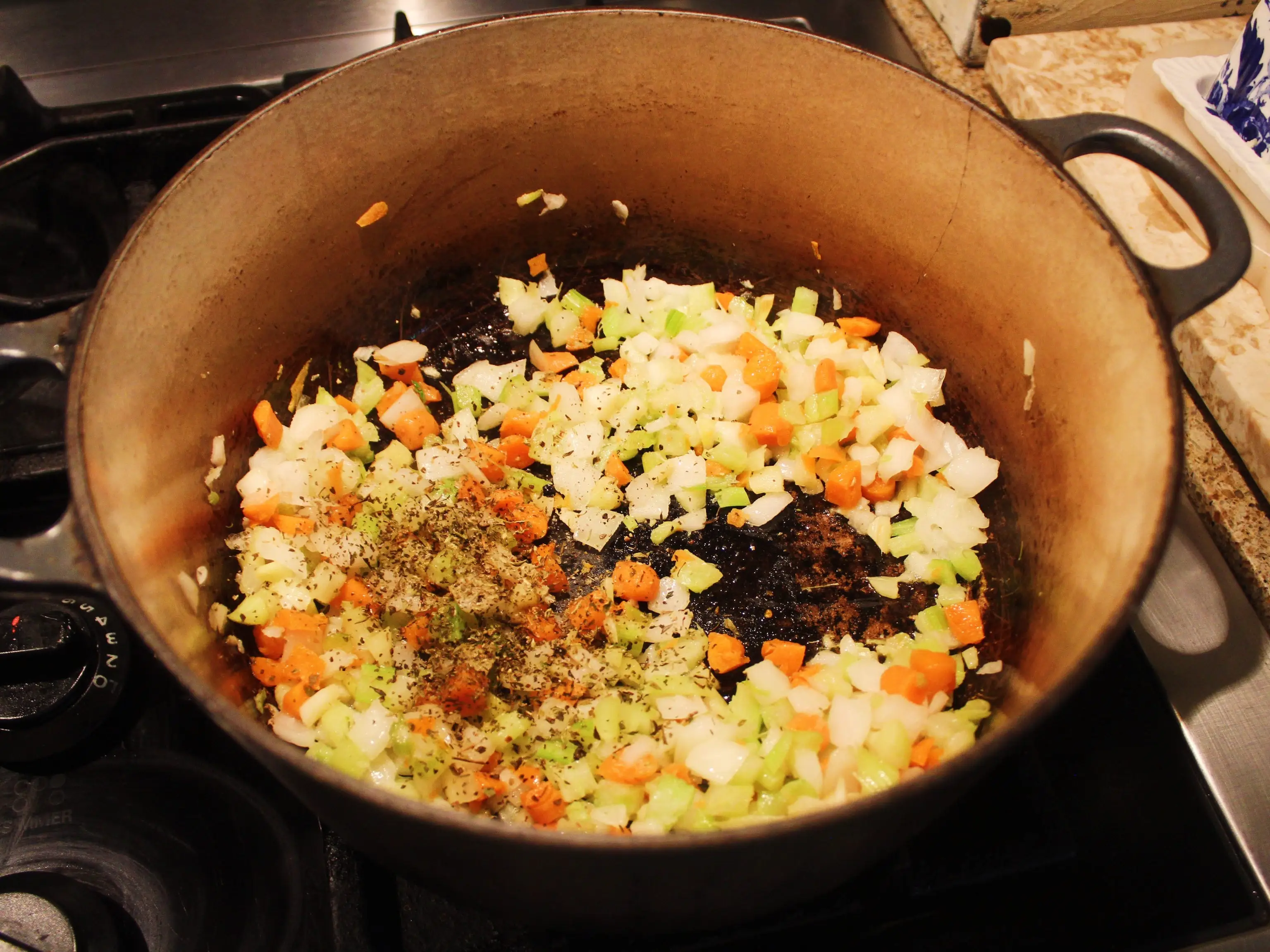 Chopped carrots, onions, and celery with seasonings cooking in a large pot on a gas stovetop.