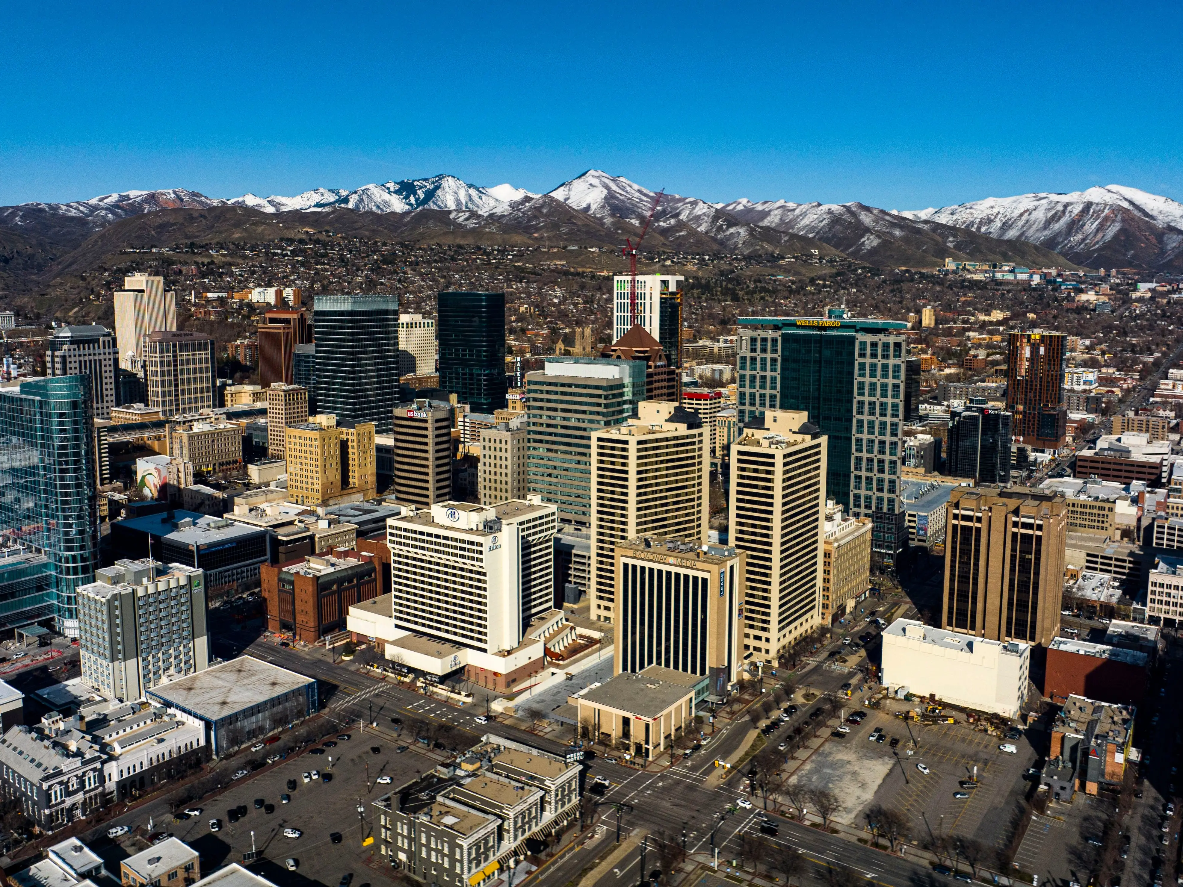 The downtown area of a city from an aerial view, with snow-capped mountains in the background.