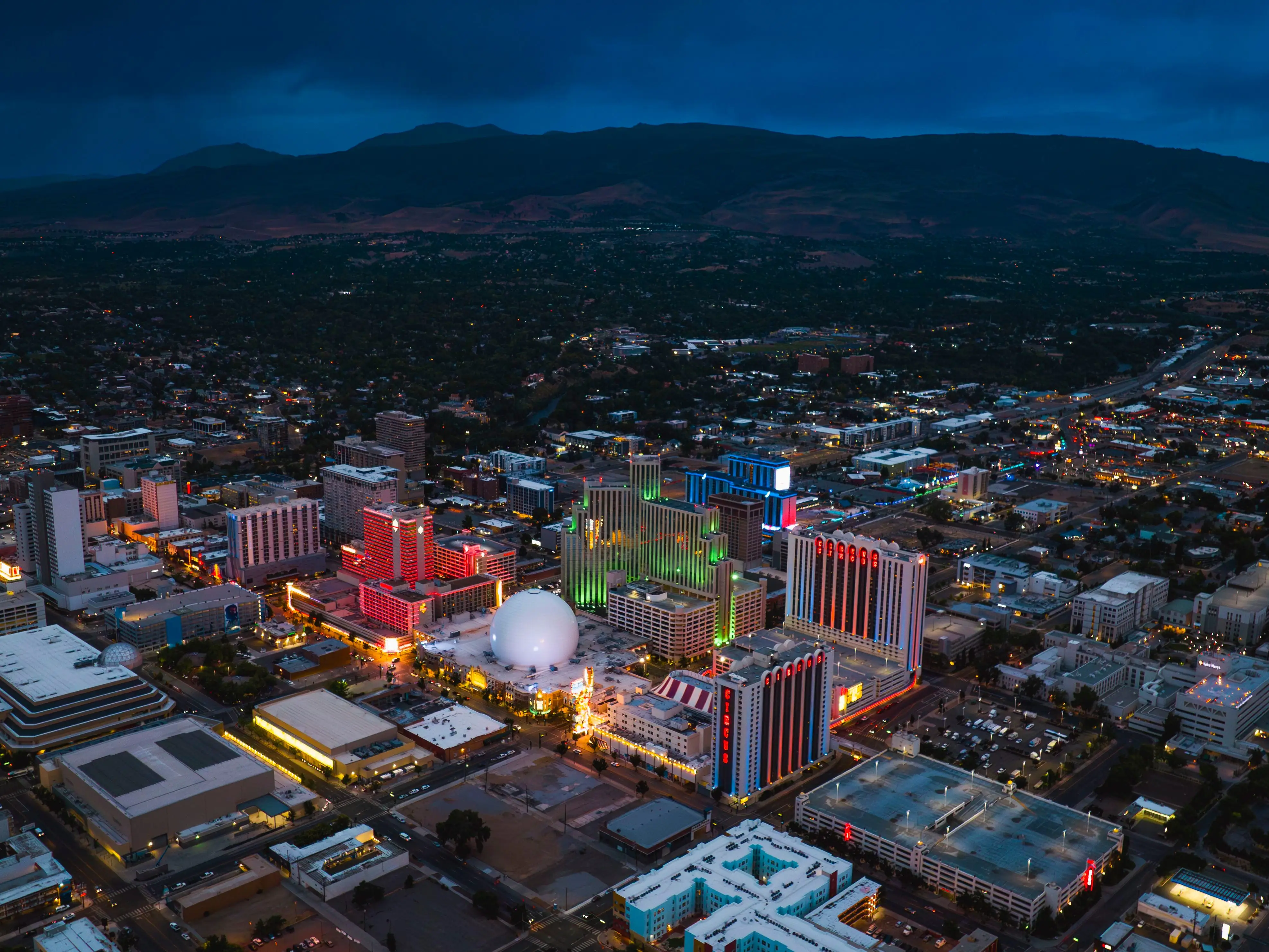 An aerial view of a city during dusk, with mountains in the background.
