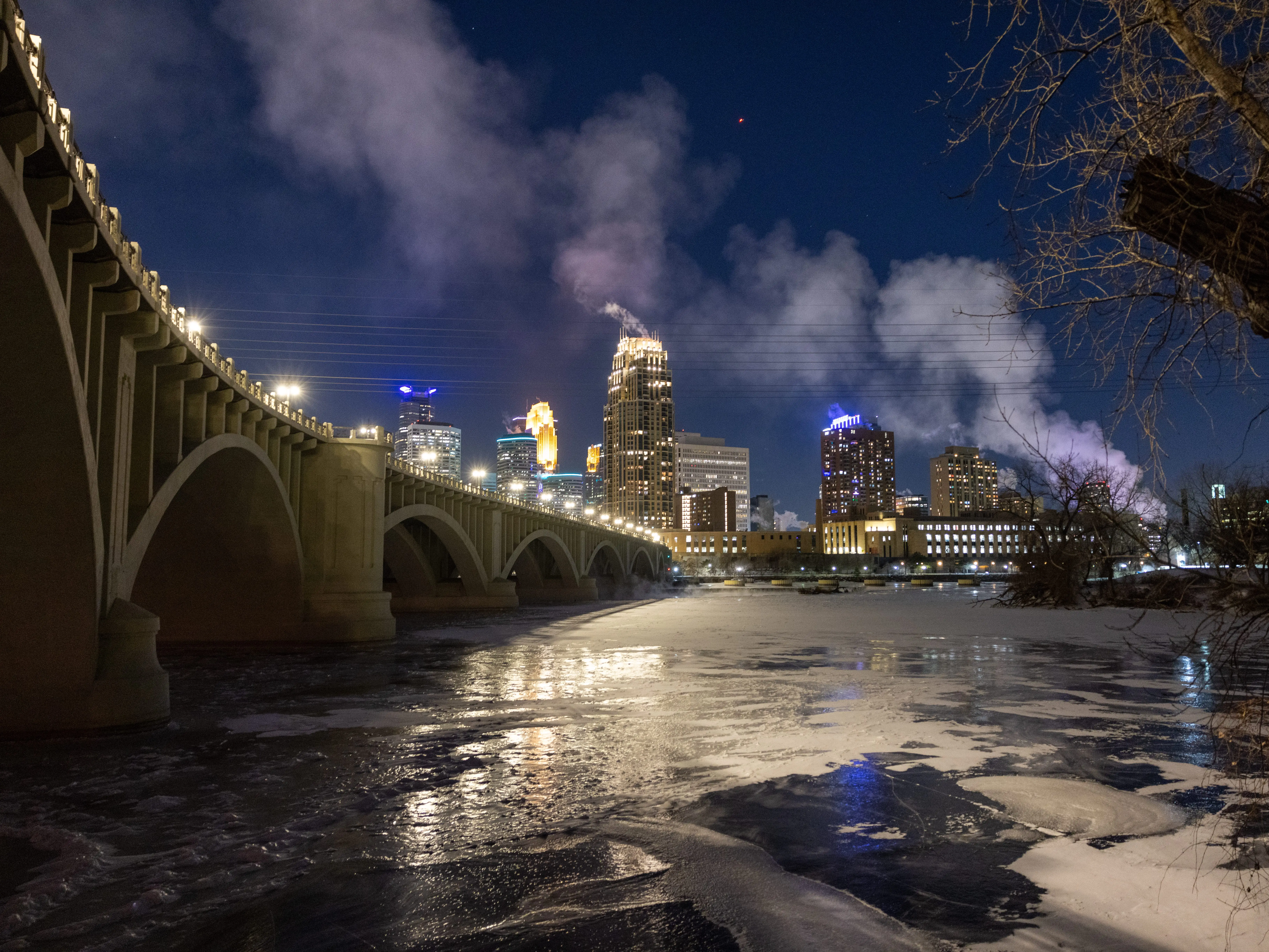 A night photo of a city skyline with an icy river in the foreground.