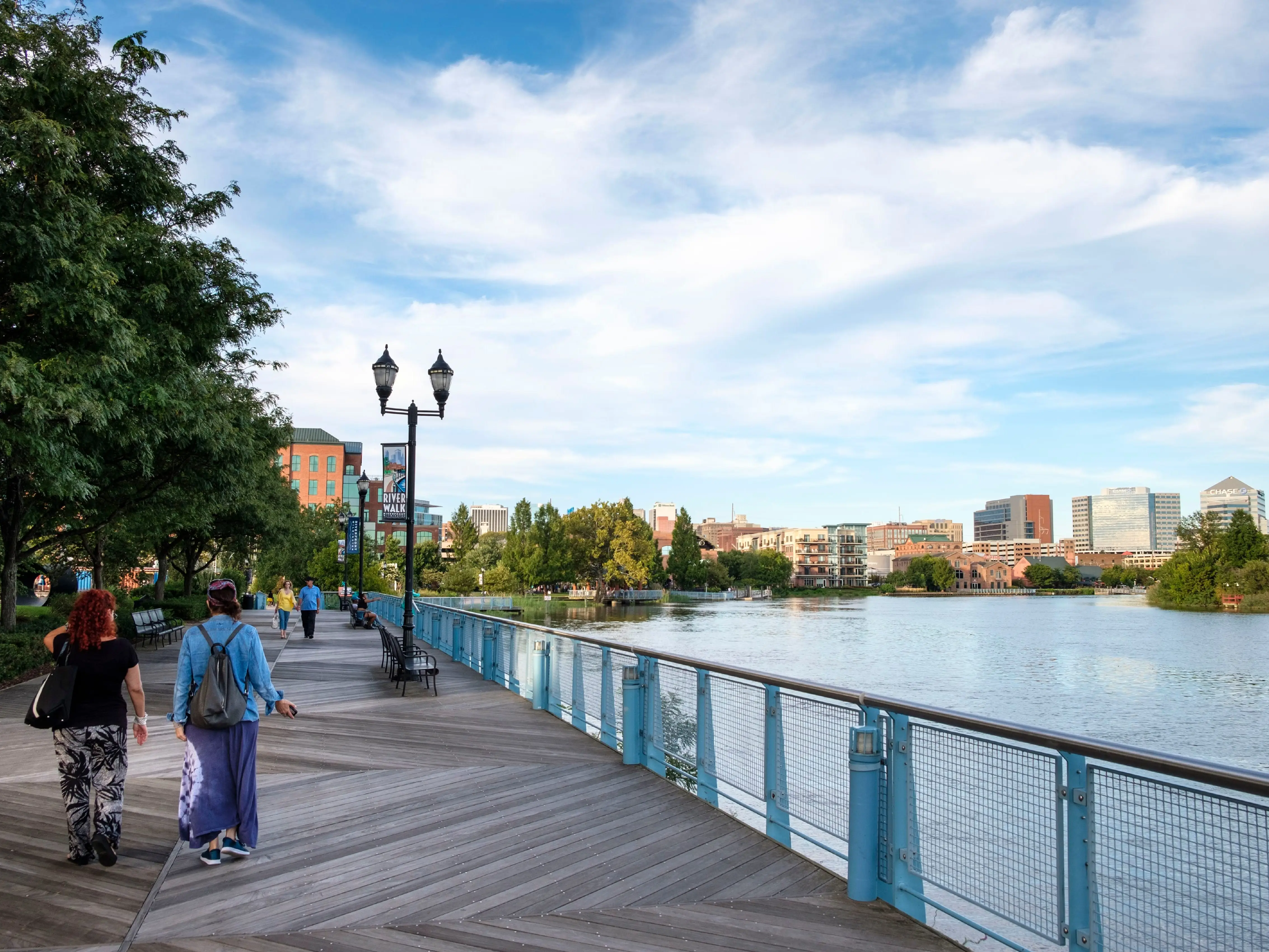 People walk on a boardwalk next to a river.