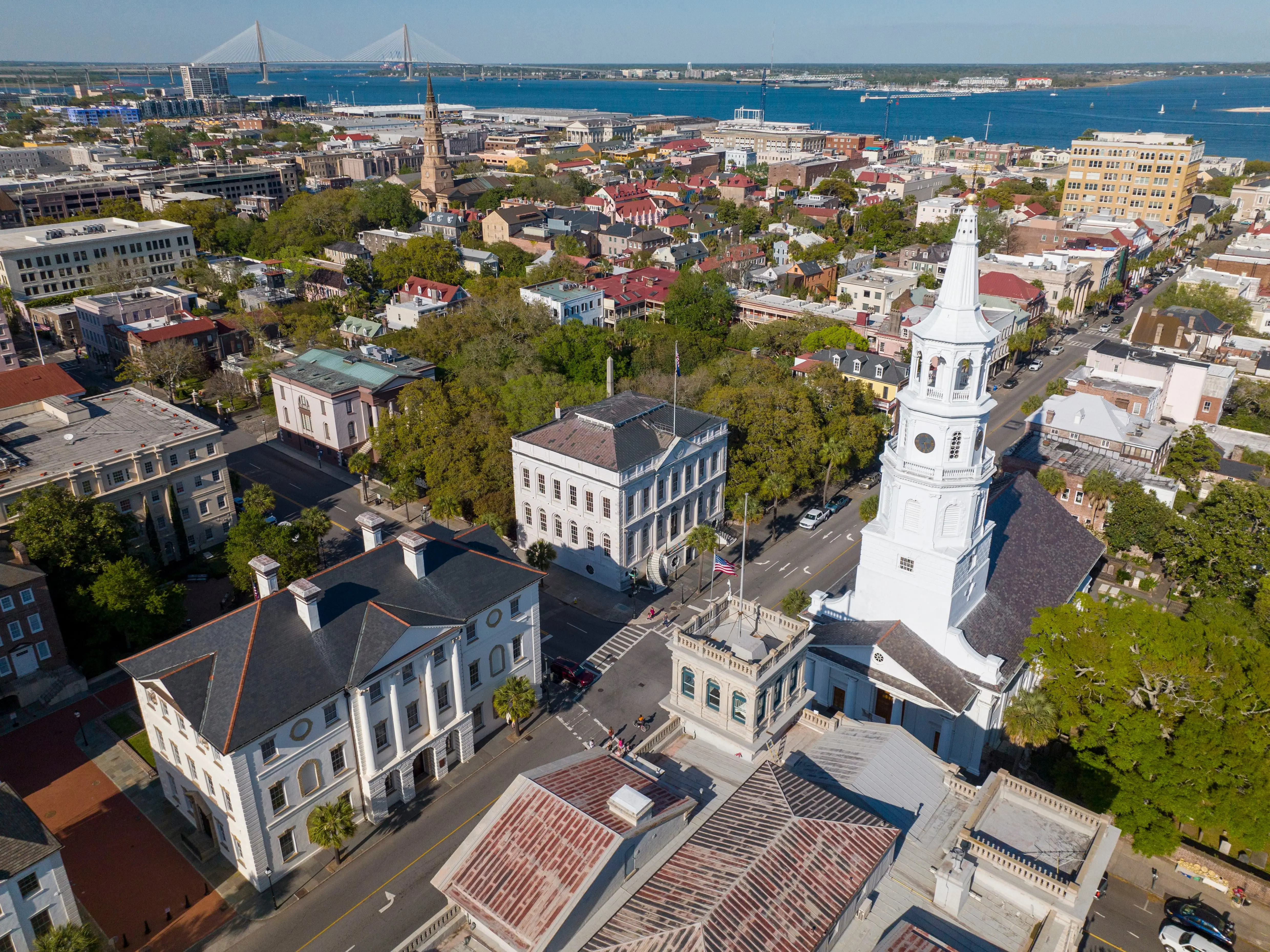 An aerial view of a small city with a church steeple in the foreground and a river in the background.