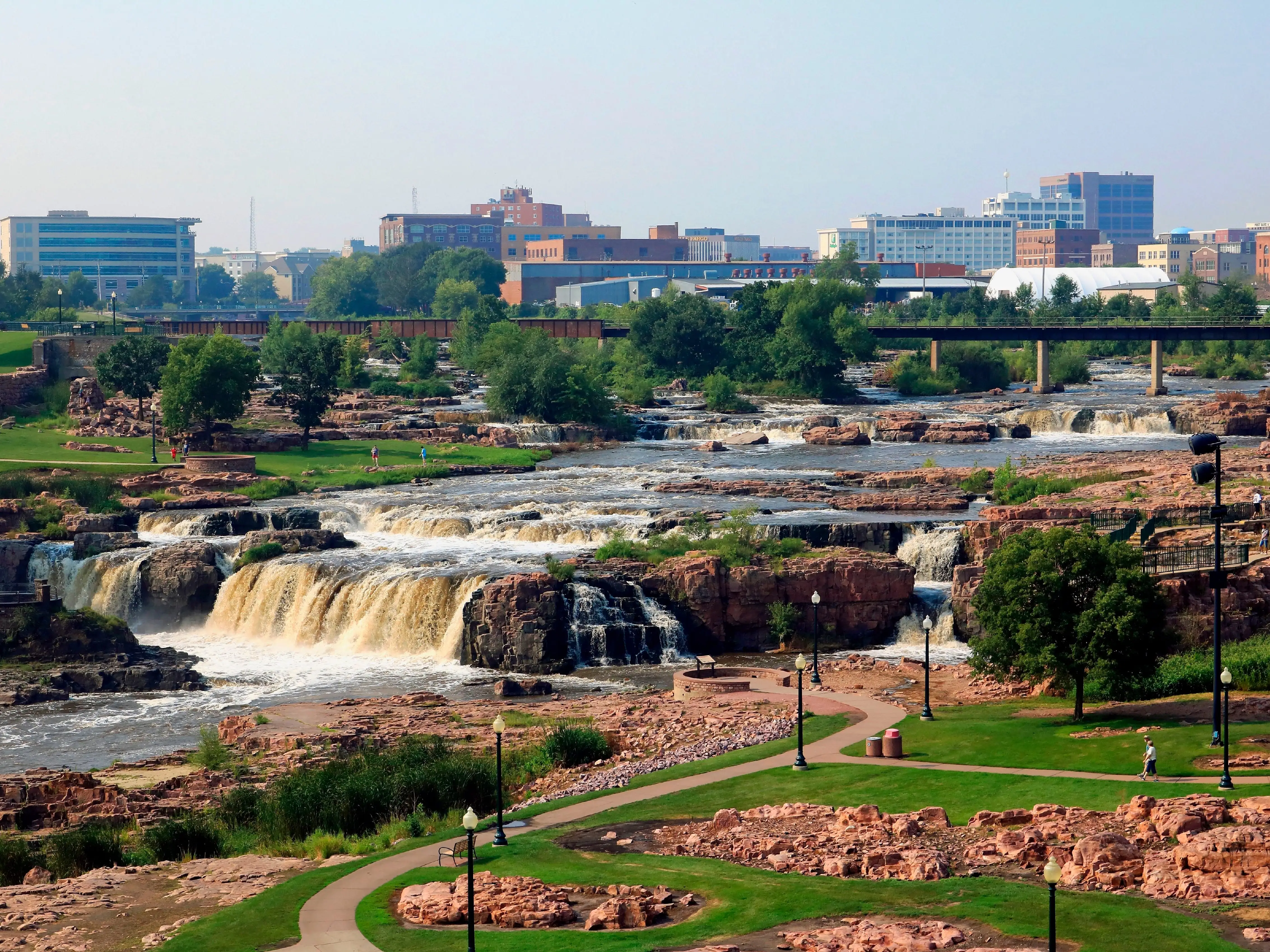A photo of a city skyline in the background with red rocks and tiered, small waterfalls in the foreground.