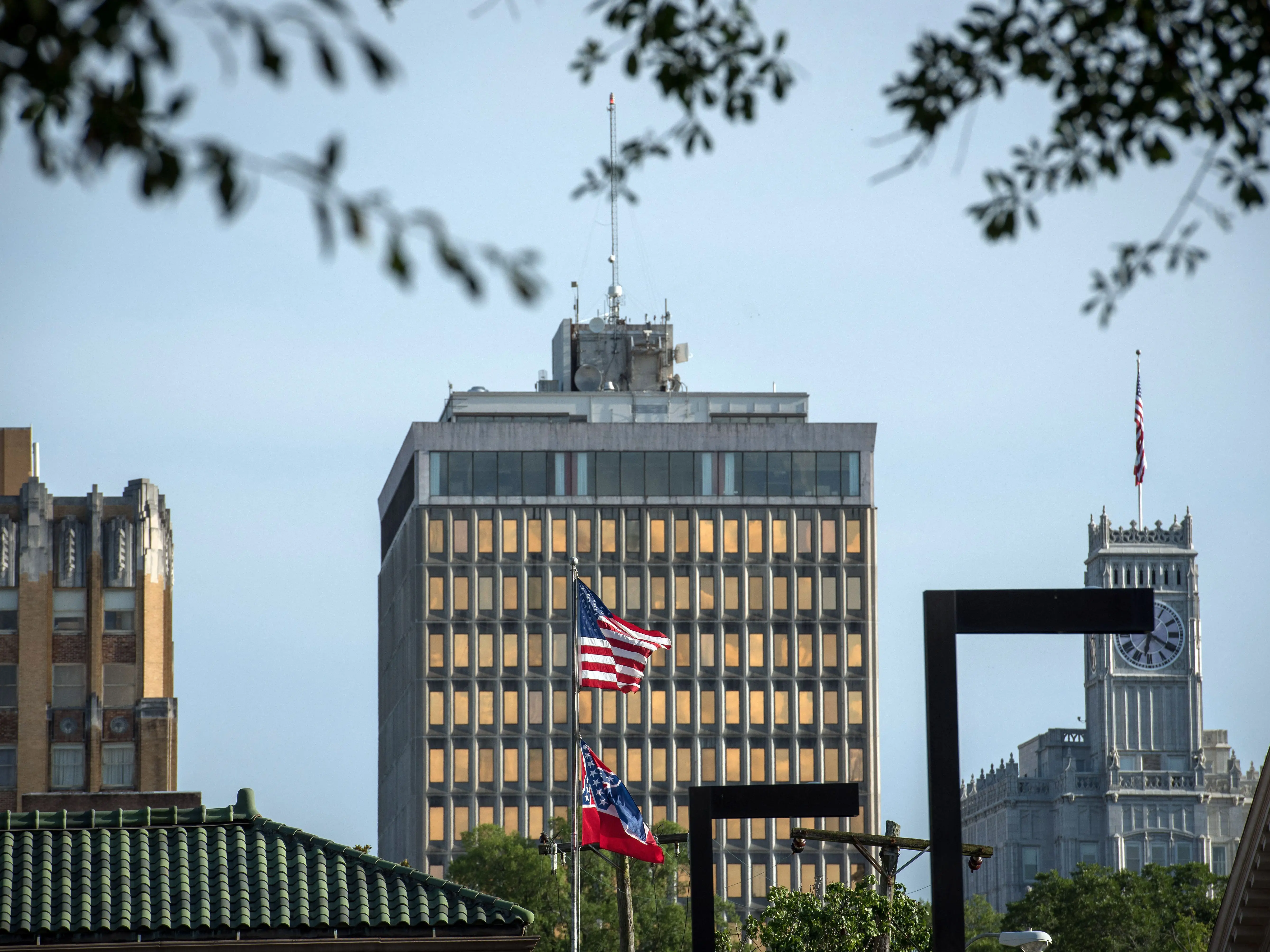 Buildings of a city stand together with an American flag waving in the foreground.