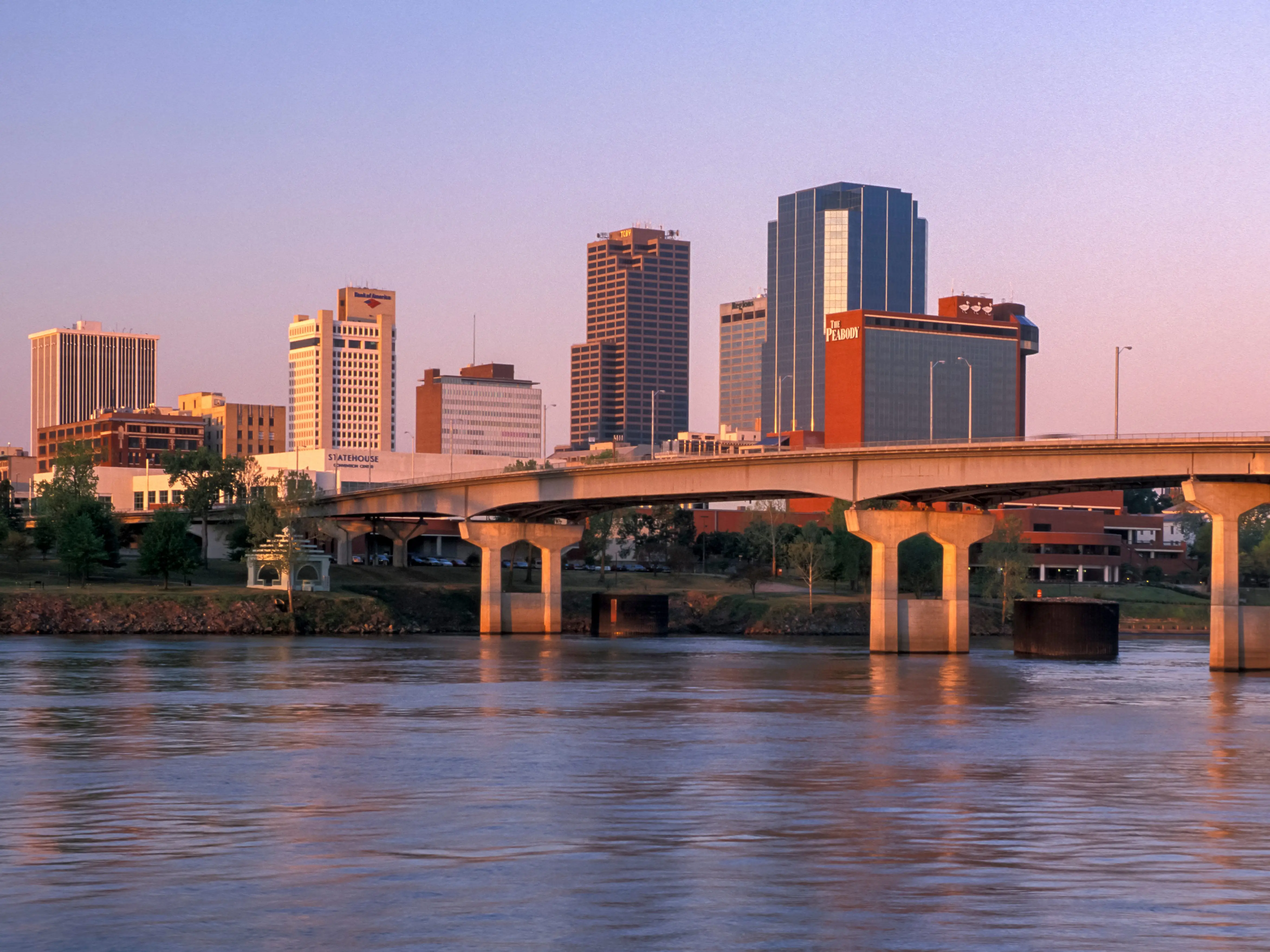 A photo of a city skyline at sunset with a river and a bridge in the foreground.