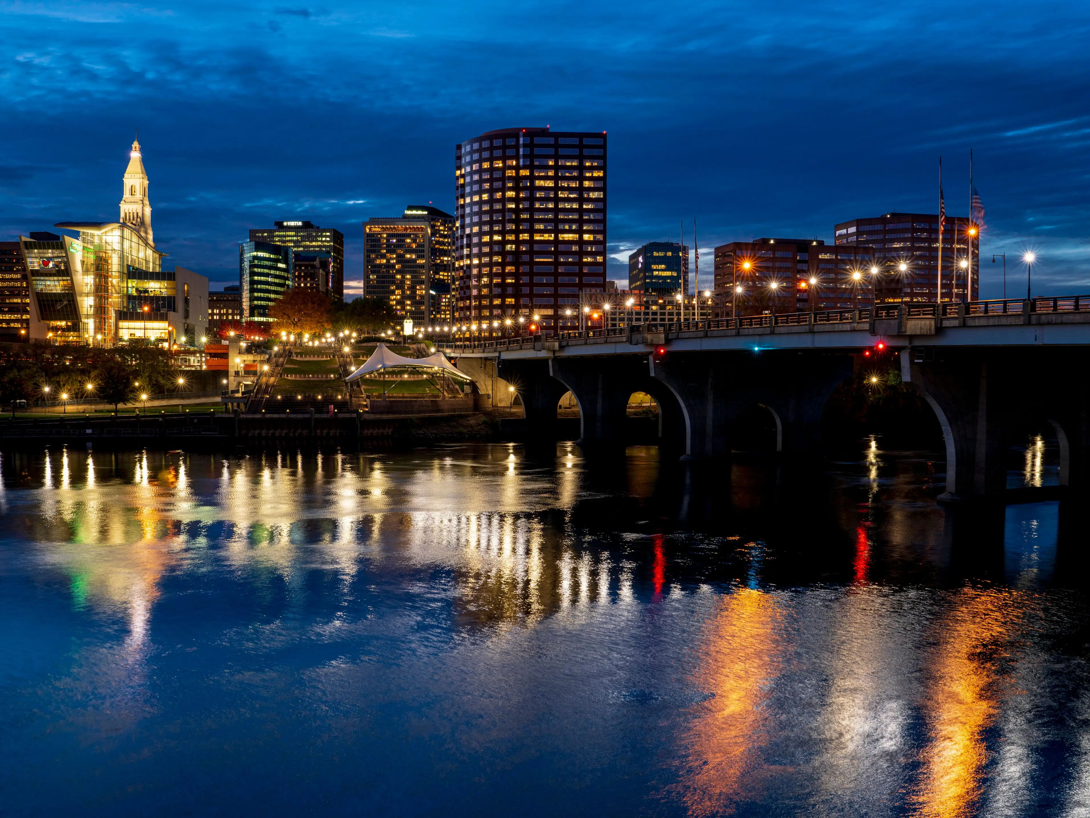 A view of a city at dusk, with a river and bridge in the foreground.