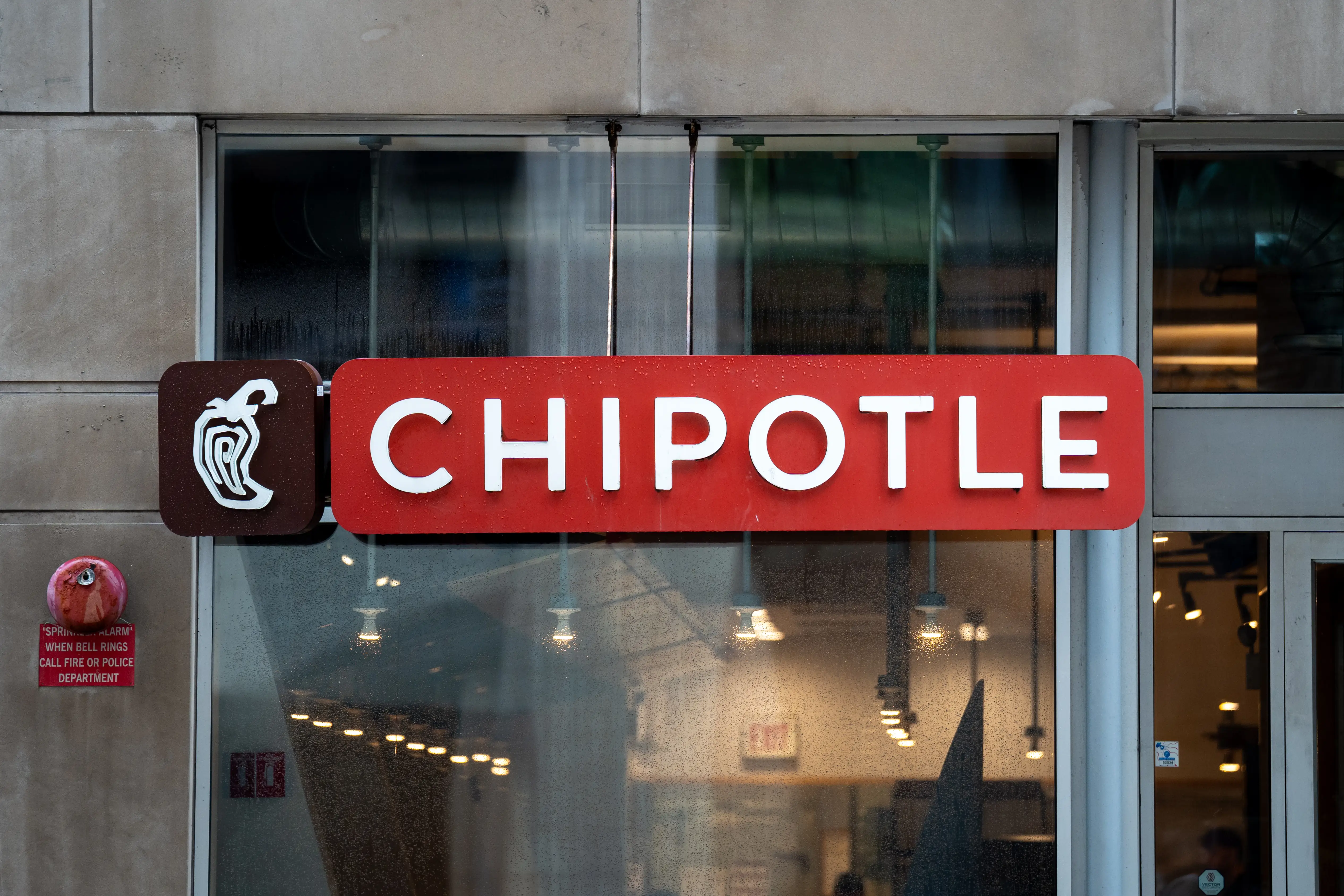 Chipotle storefront sign with white lettering on a red panel above glass windows.