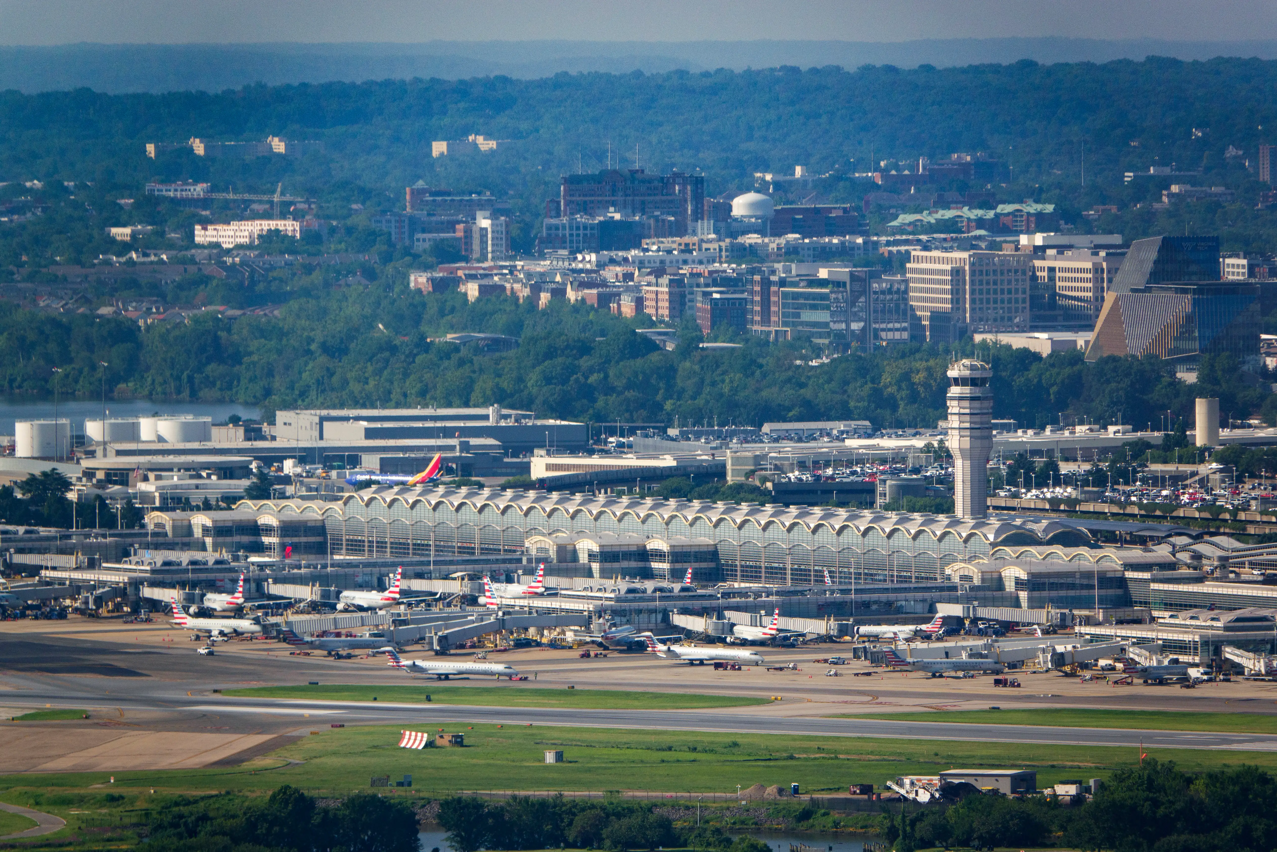 An aerial view of Ronald Reagan Washington National Airport is seen on August 6, 2026, in Arlington, Virginia with runways, control tower, aircraft, and surrounding wooded office areas.