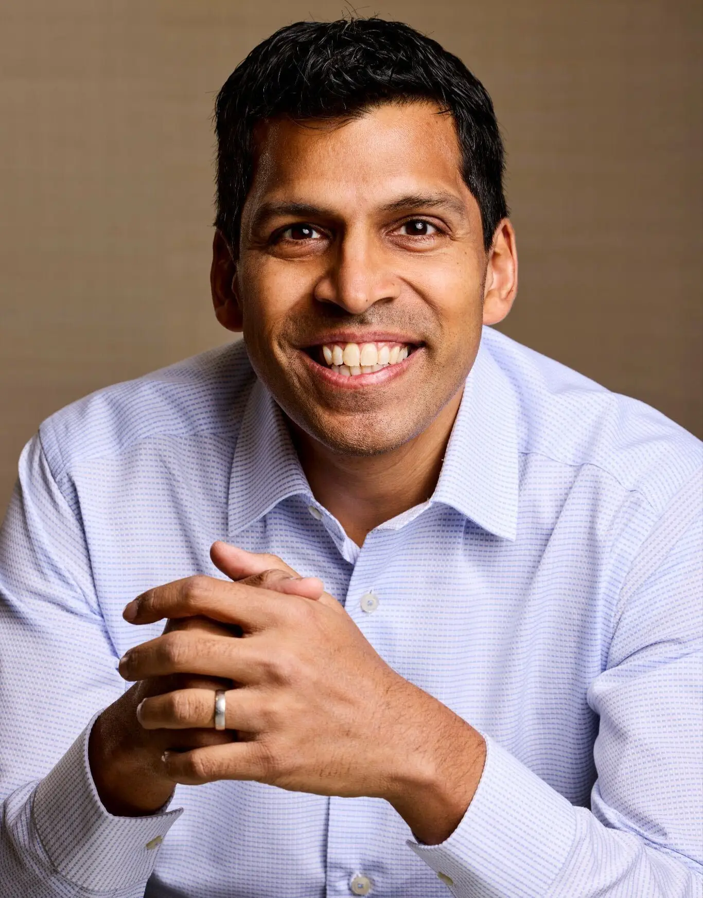 A man wearing a light colored button-down shirt smiles