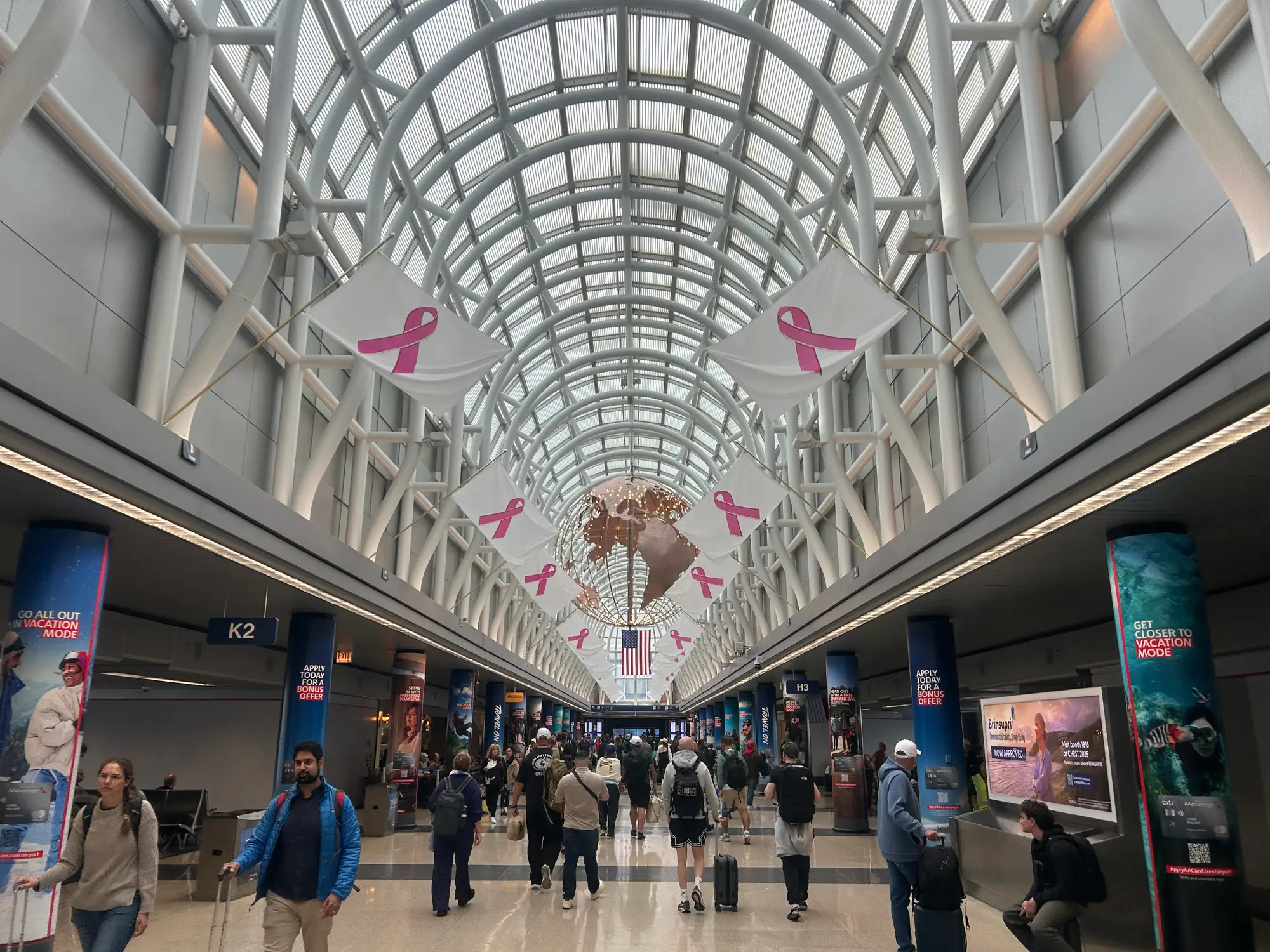 Travelers walk through the Chicago O'Hare International concourse decorated with pink ribbon banners and an American flag.