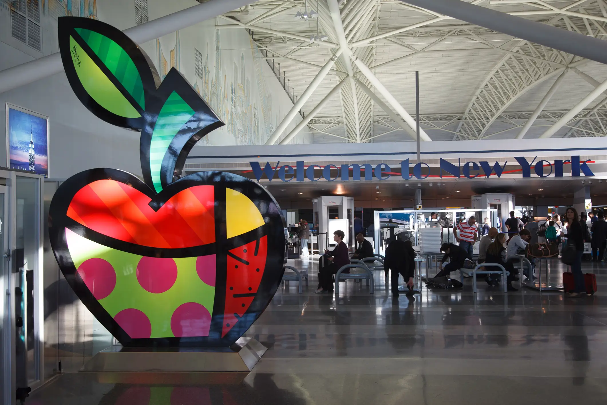 Colorful apple sculpture stands inside JFK airport terminal near a large 