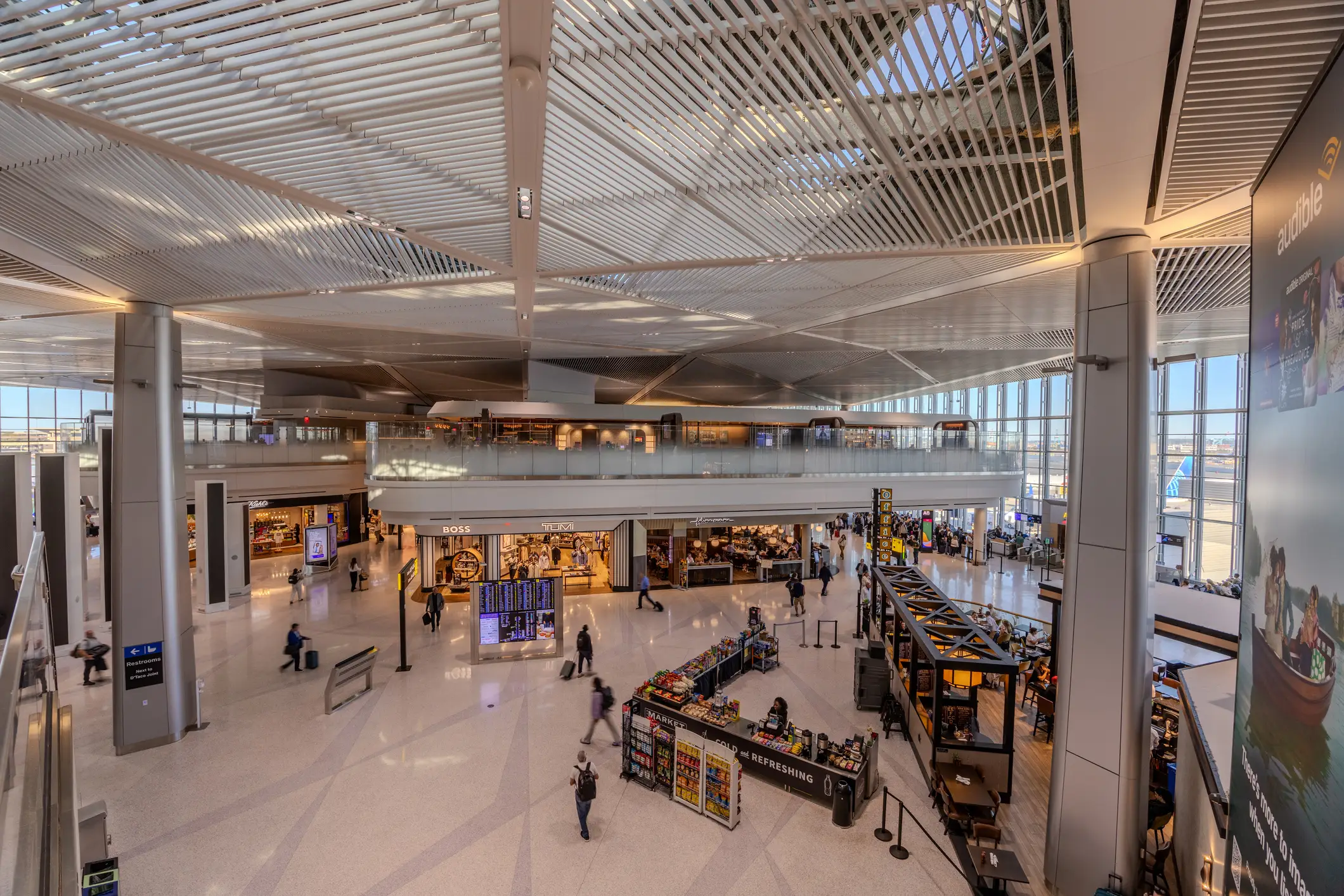 Spacious airport terminal hall at Newark Liberty International Airport with travelers, retail shops, kiosks, flight display boards, and a high ribbed ceiling.