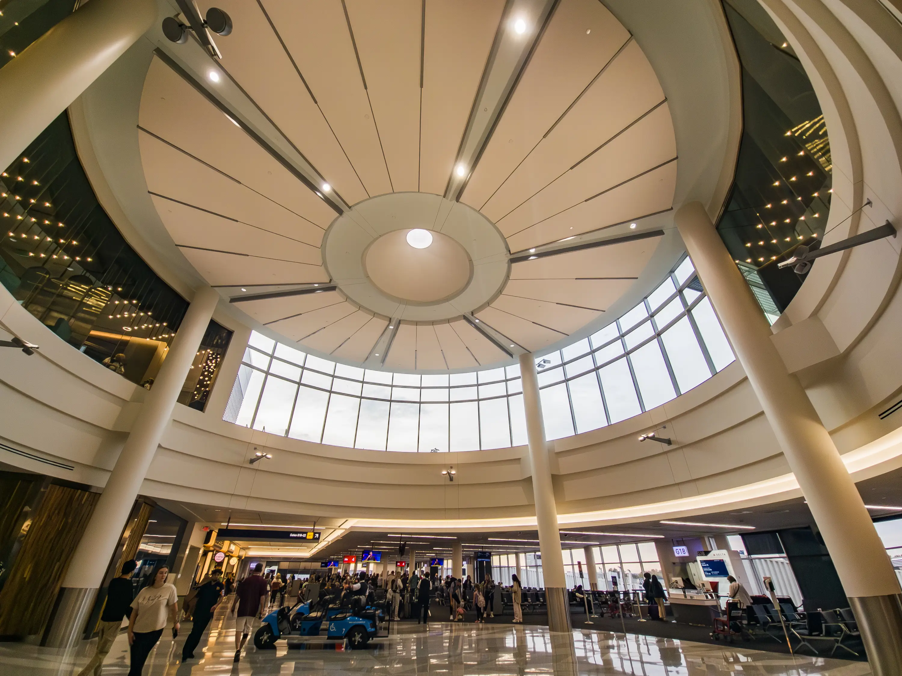 Spacious airport terminal concourse at Minneapolis-Saint Paul International Airport with a circular skylight ceiling, columns, passengers, seating, and gate G18 signage.