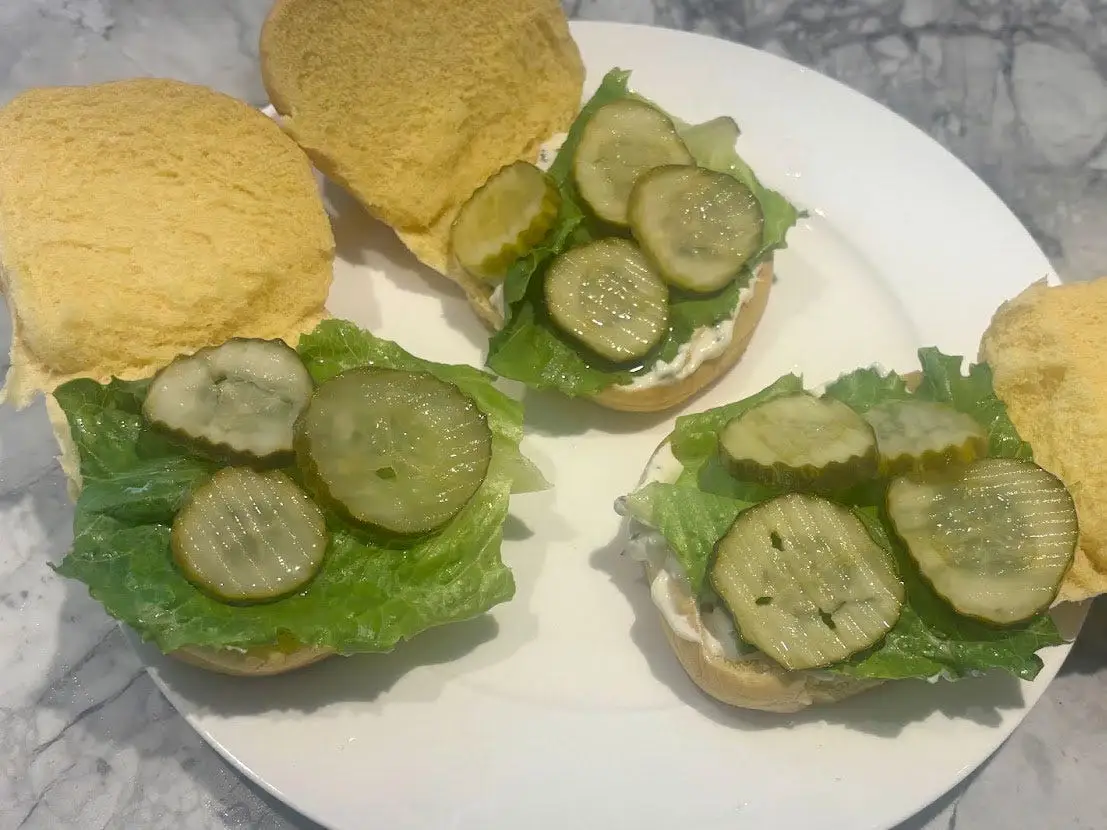 Three rolls with mayo, lettuce, and pickles on a plate.