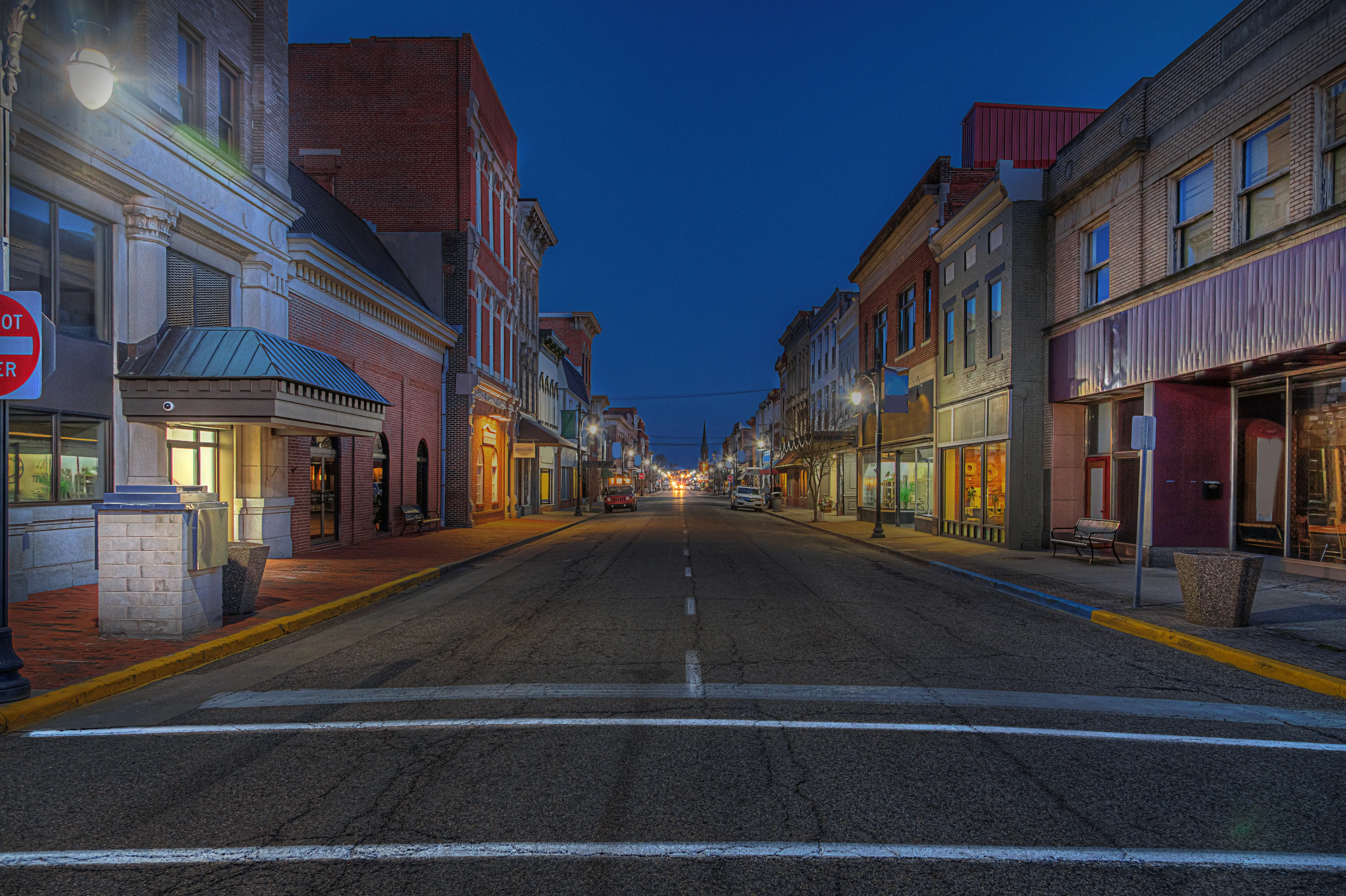 Quiet downtown street in Vincennes, Indiana, at dusk, lined with illuminated storefronts and brick buildings.