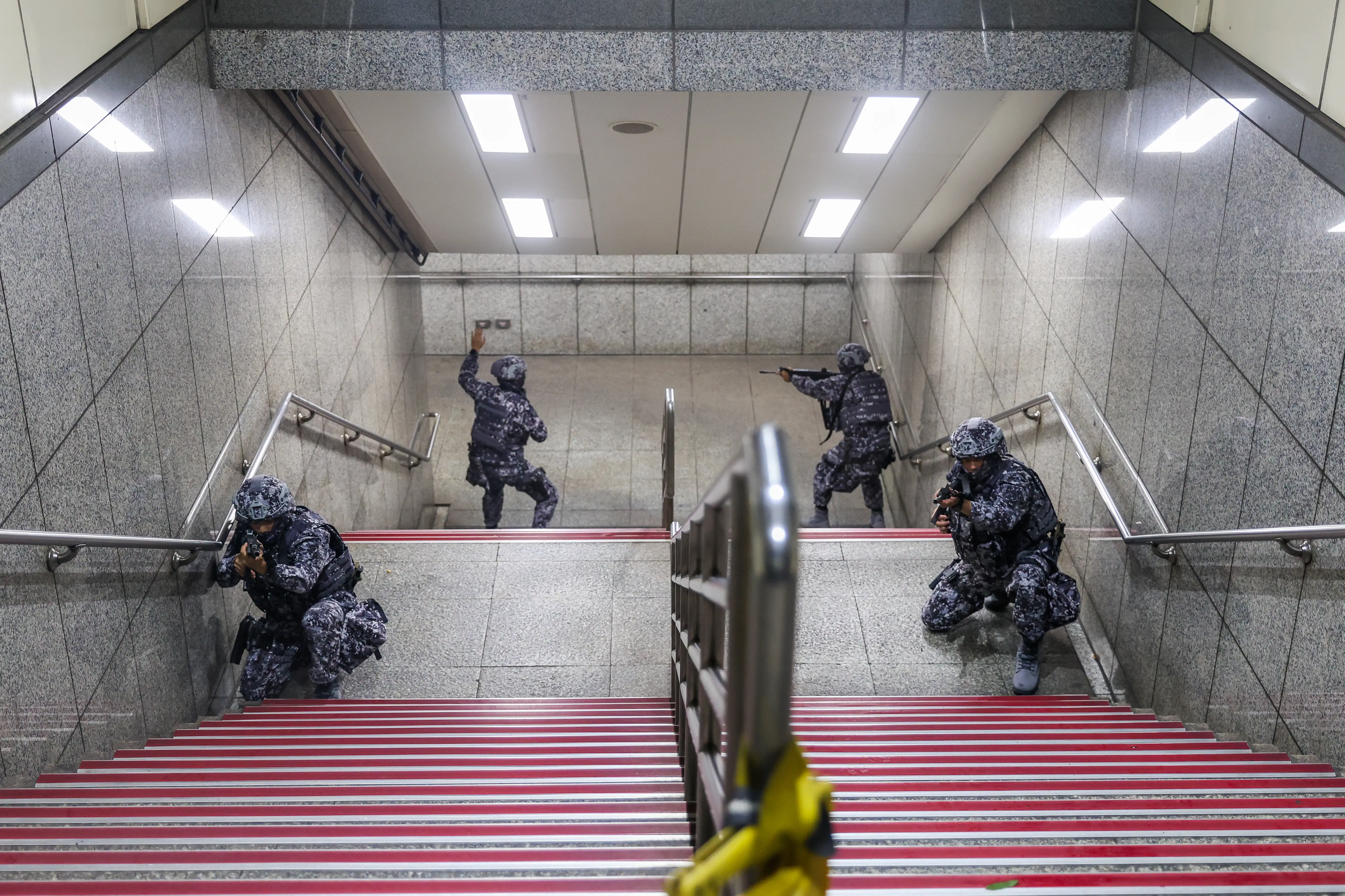 Four Taiwanese infantry in digital camo take position in a subway station stairwell.
