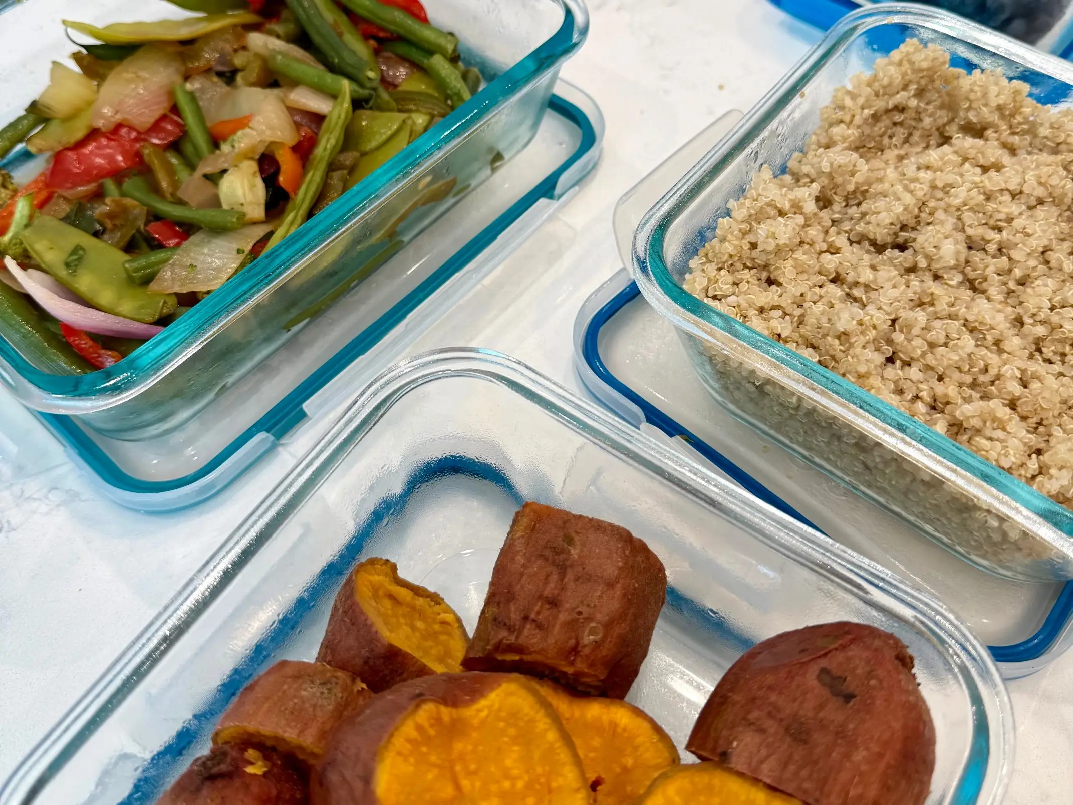 Clear storage containers filled with veggies, grains, potatoes, and fruits.