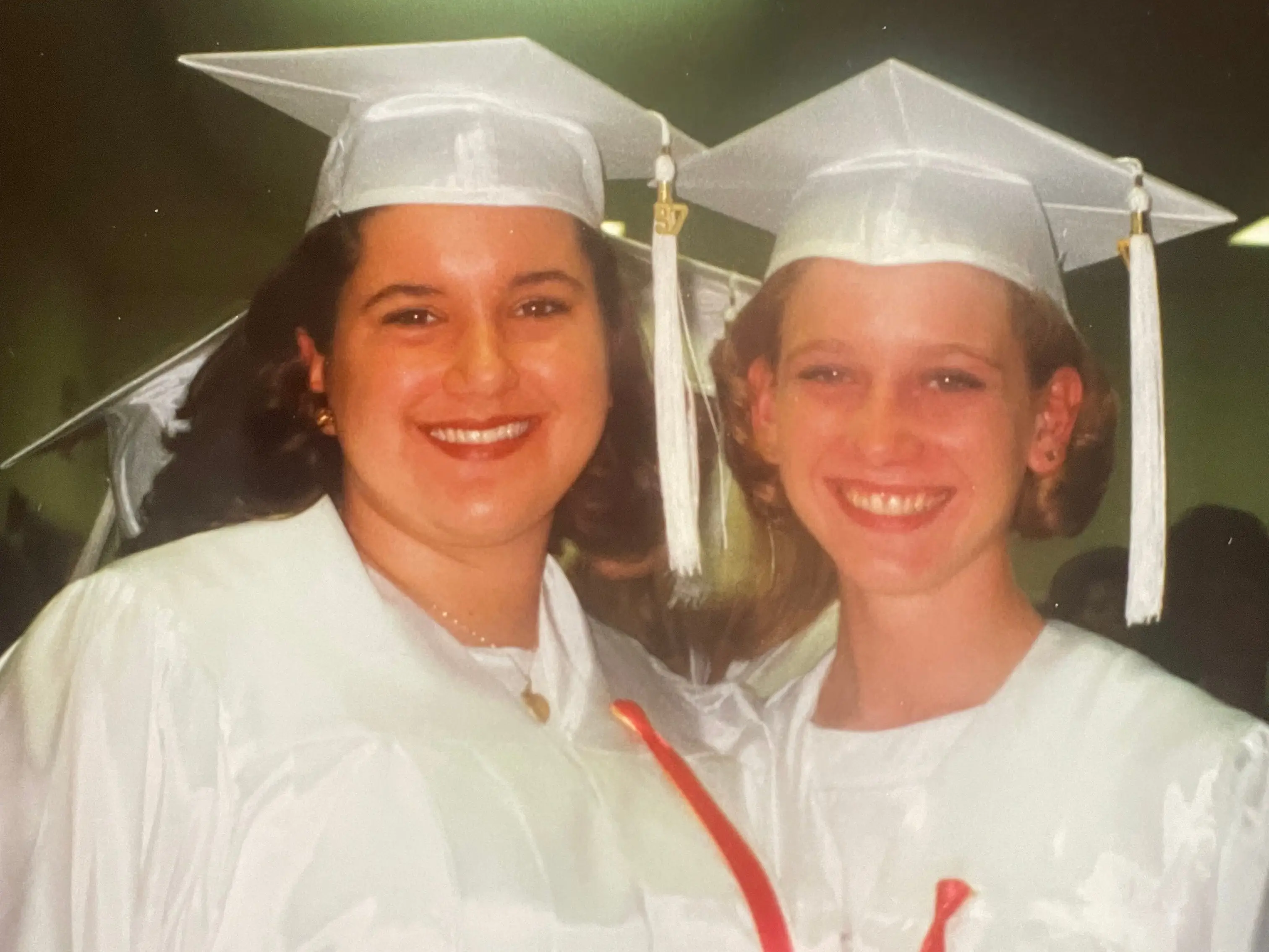 Two girls in white graduation caps and gowns, smiling