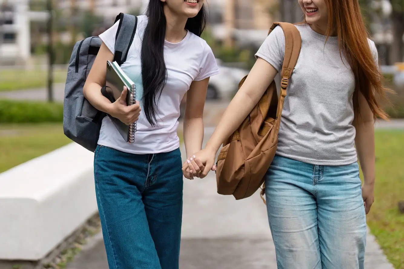 Two girls with backpacks, jeans, t shirts, holding hands and smiling