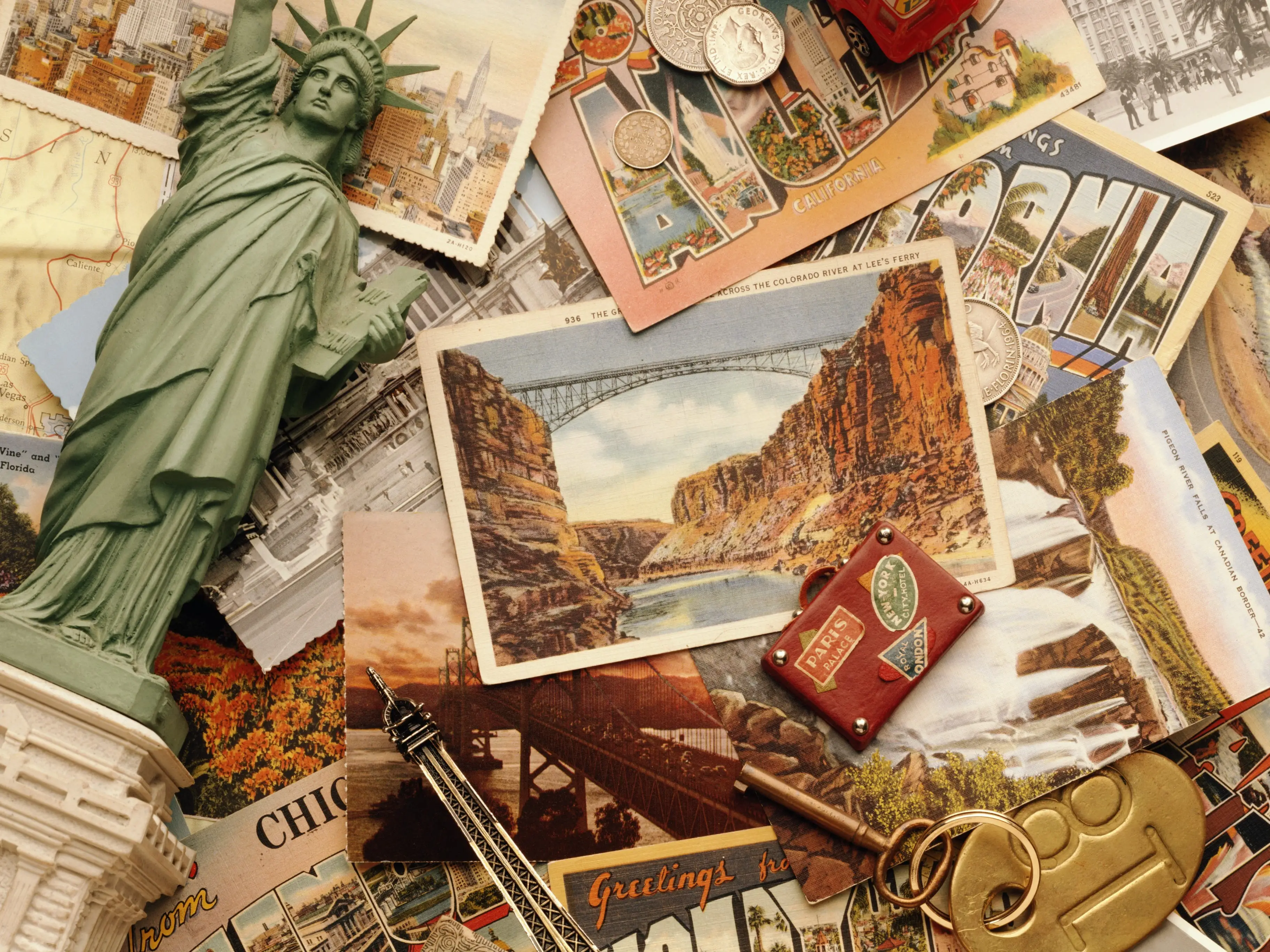 Travel souvenirs and postcards surround a miniature Statue of Liberty, Eiffel Tower, red bus, coins, and luggage tags.