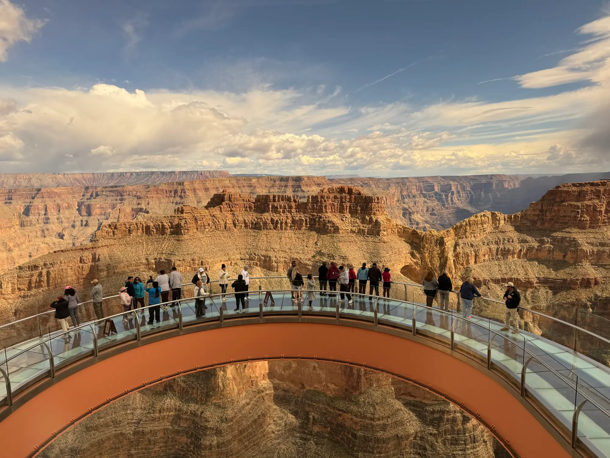 Visitors stand on a glass skywalk overlooking a sunlit canyon in Grand Canyon National Park.